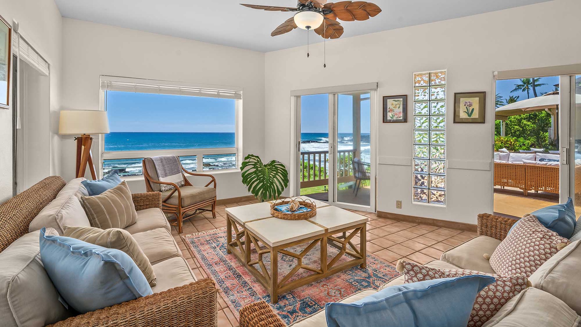 Your oceanfront living room invites you to unwind with stunning sea views through expansive windows and doors, tropical breezes from the ceiling fan, and comfortable coastal furnishings perfect for relaxing.