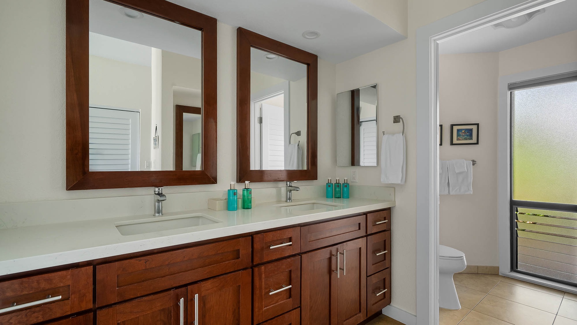 Step into your private bathroom featuring elegant dual vanities with rich wood cabinetry, pristine white countertops, and a separate toilet area for added convenience.