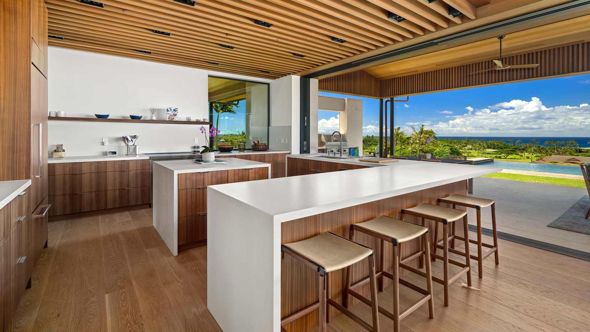 Bright modern kitchen with sleek wood cabinetry and ocean views, opening seamlessly to your private pool and terrace—perfect for entertaining or relaxing with island breezes.