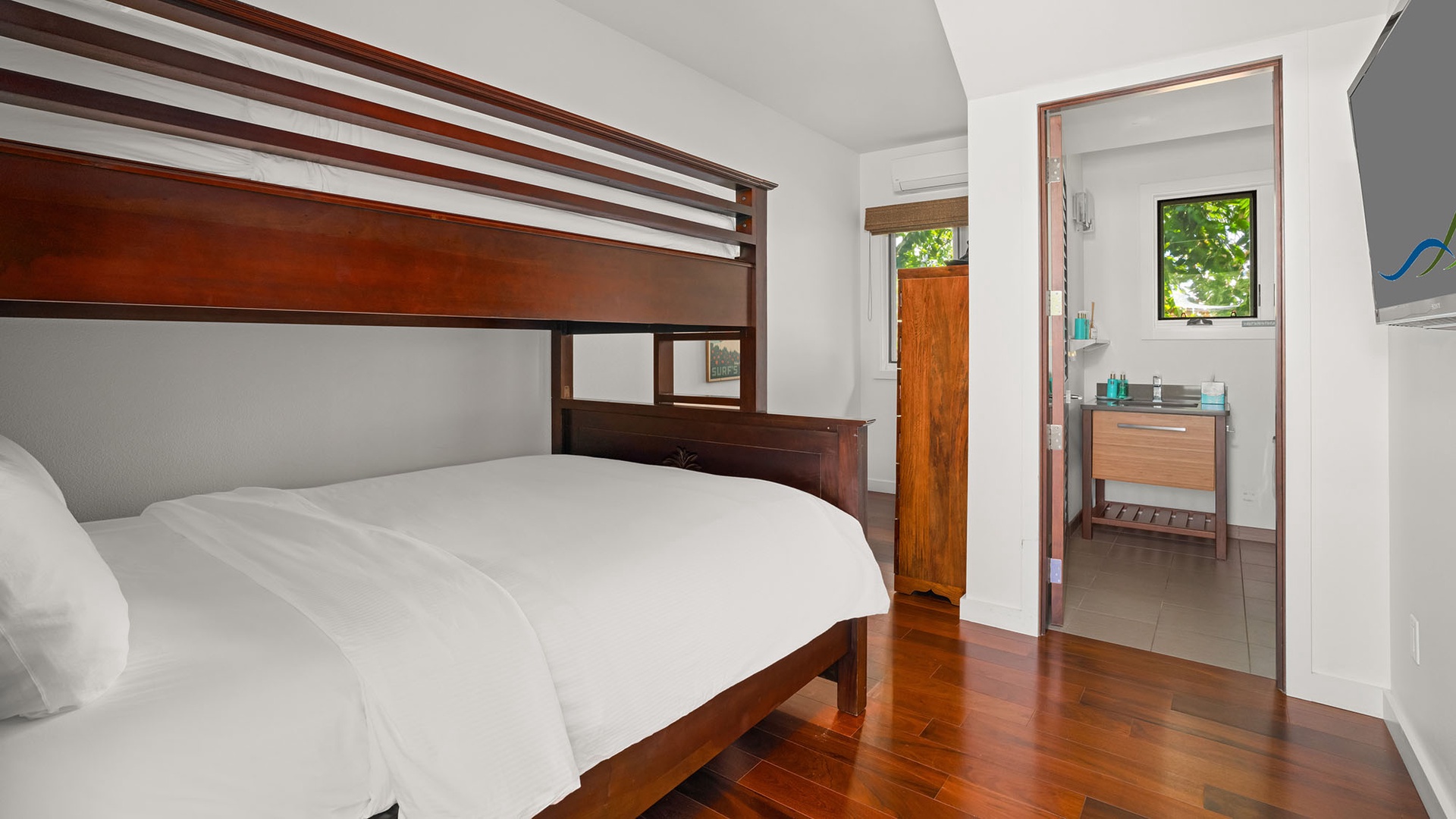 Your cozy bedroom features a comfortable queen bed with a bunk above, rich wood floors, and an ensuite bathroom with natural light, perfect for families or groups.