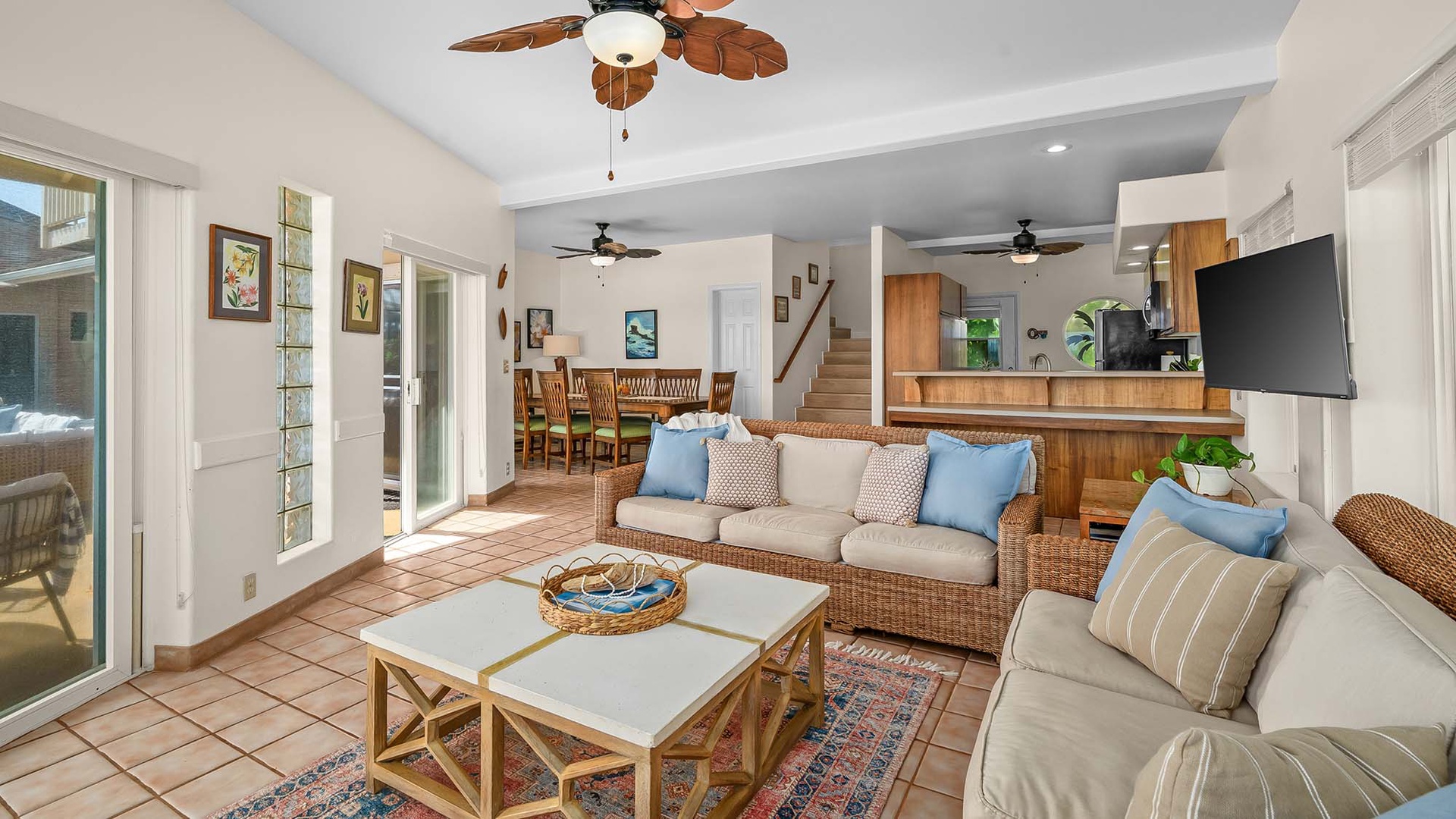Step into your bright, open-plan living space where tropical charm meets comfort. Rattan sofas invite you to unwind while ceiling fans keep the breeze flowing, and natural light pours through glass doors opening to your private patio.