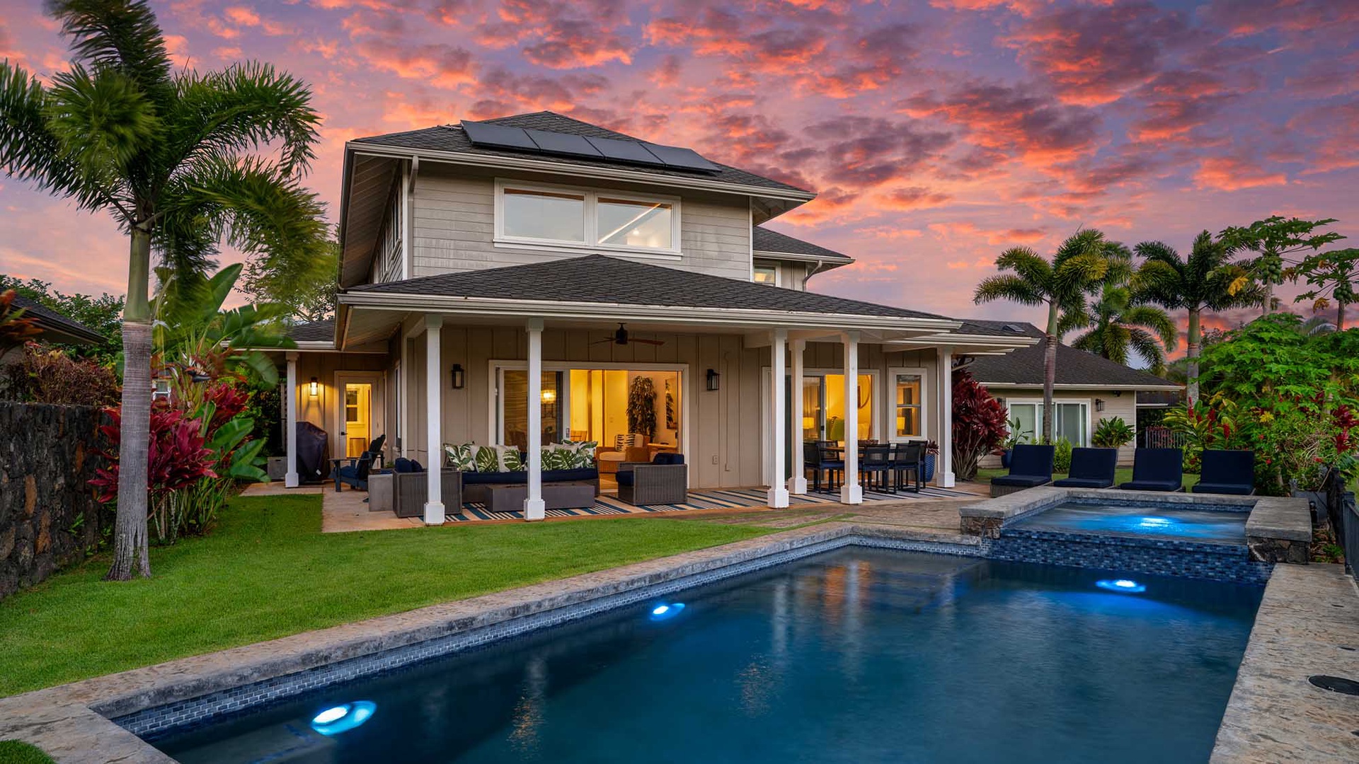 A stunning tropical property featuring a private pool with integrated spa, surrounded by lush palm trees and manicured lawn. Captured at dusk beneath a dramatic sunset sky.
