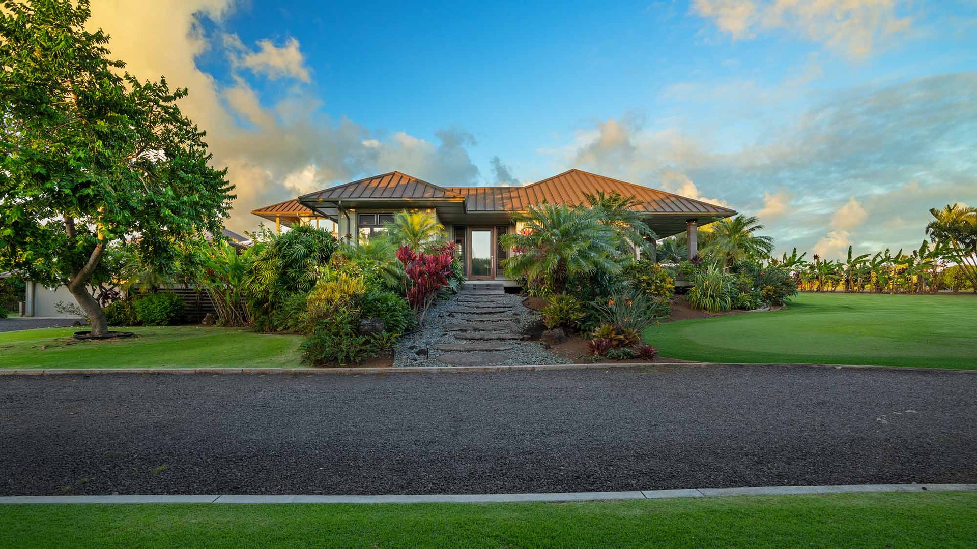 A tropical vacation home featuring lush landscaping and a welcoming entrance path, situated in a peaceful residential setting with vibrant greenery and open lawns.