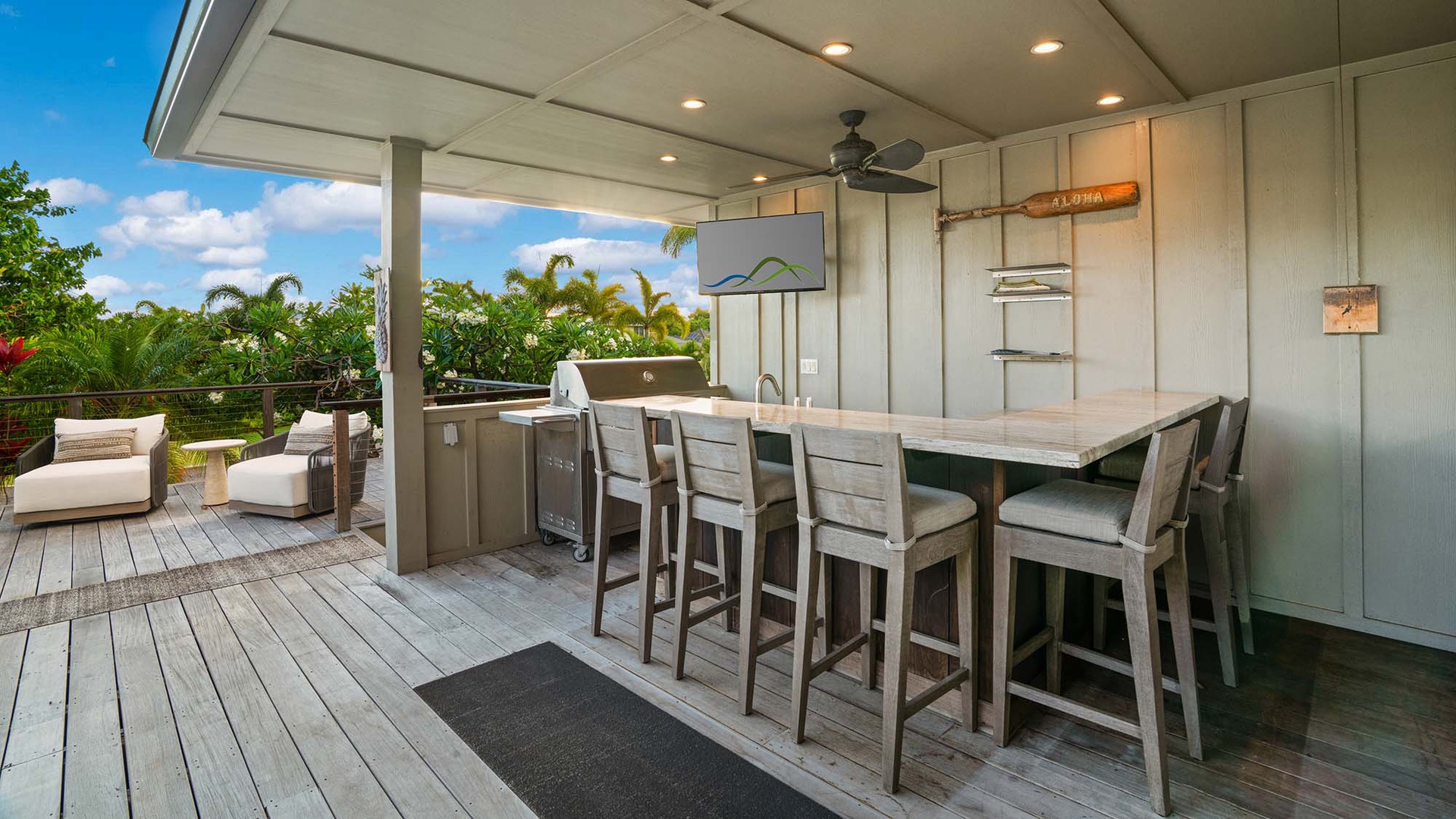 An outdoor kitchen and bar area on a covered deck, perfect for entertaining while enjoying tropical breezes and lush garden views in the background.