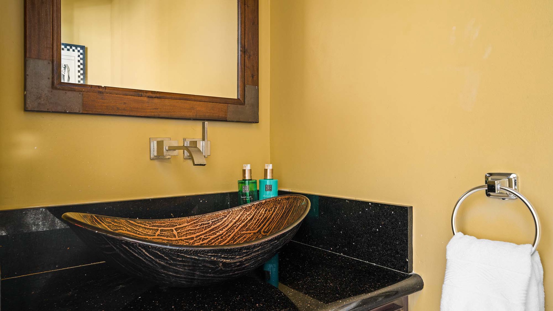 Step into your beautifully appointed bathroom featuring a stunning glass vessel sink and warm golden walls.
