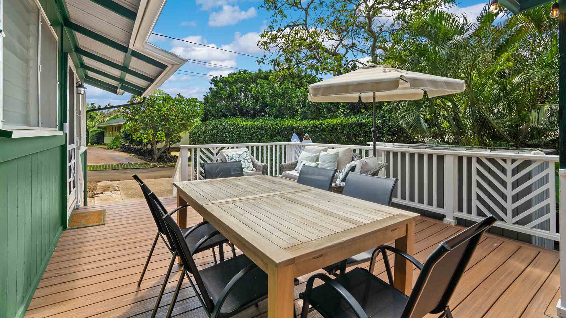Your private deck awaits with a dining table for outdoor meals, a cozy seating area under a shade umbrella, and lush tropical greenery all around.