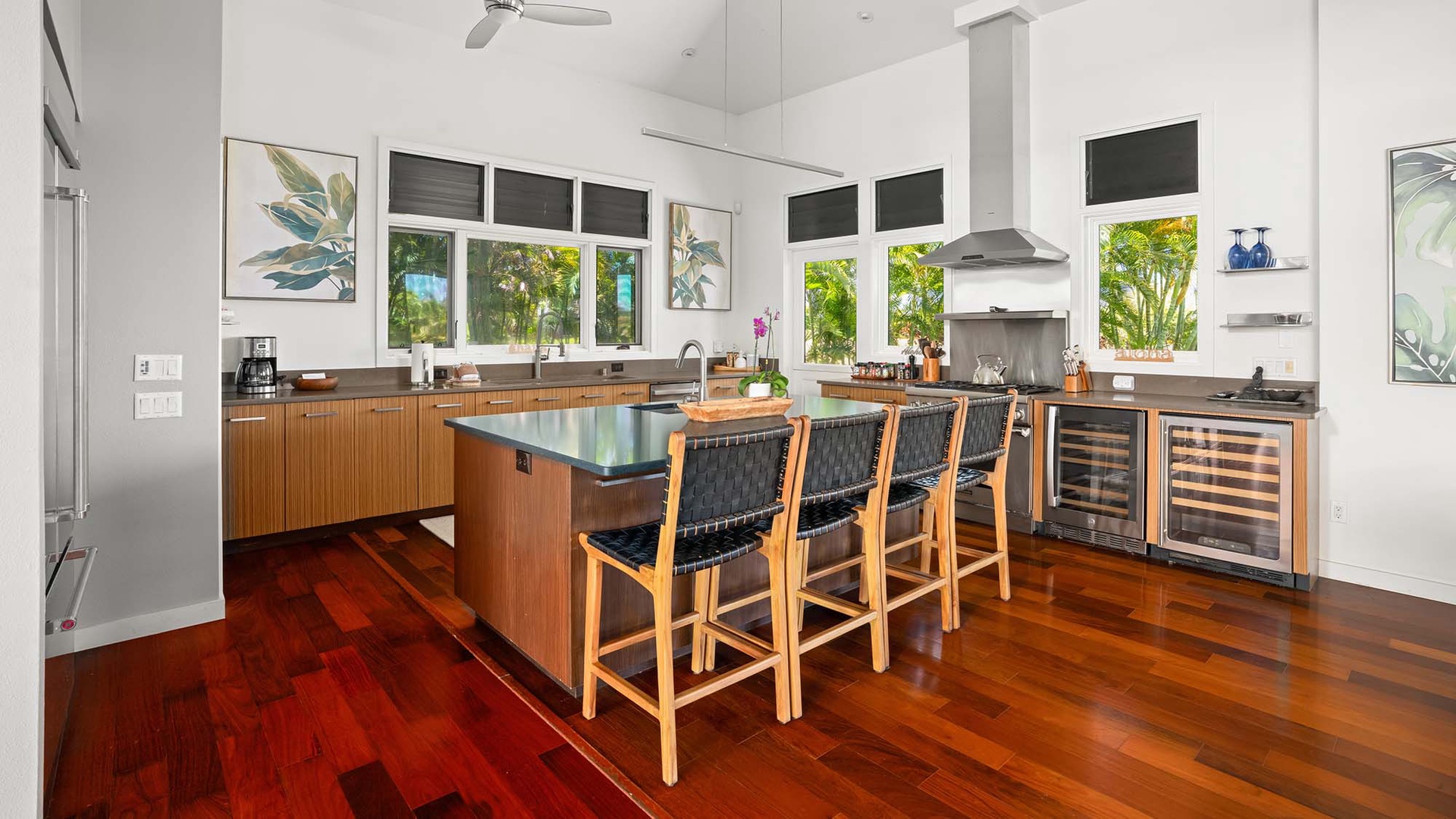 Your gourmet kitchen features rich hardwood floors, sleek cabinetry, and a spacious island perfect for gathering with family. Natural light pours through large windows, framing lush tropical views.