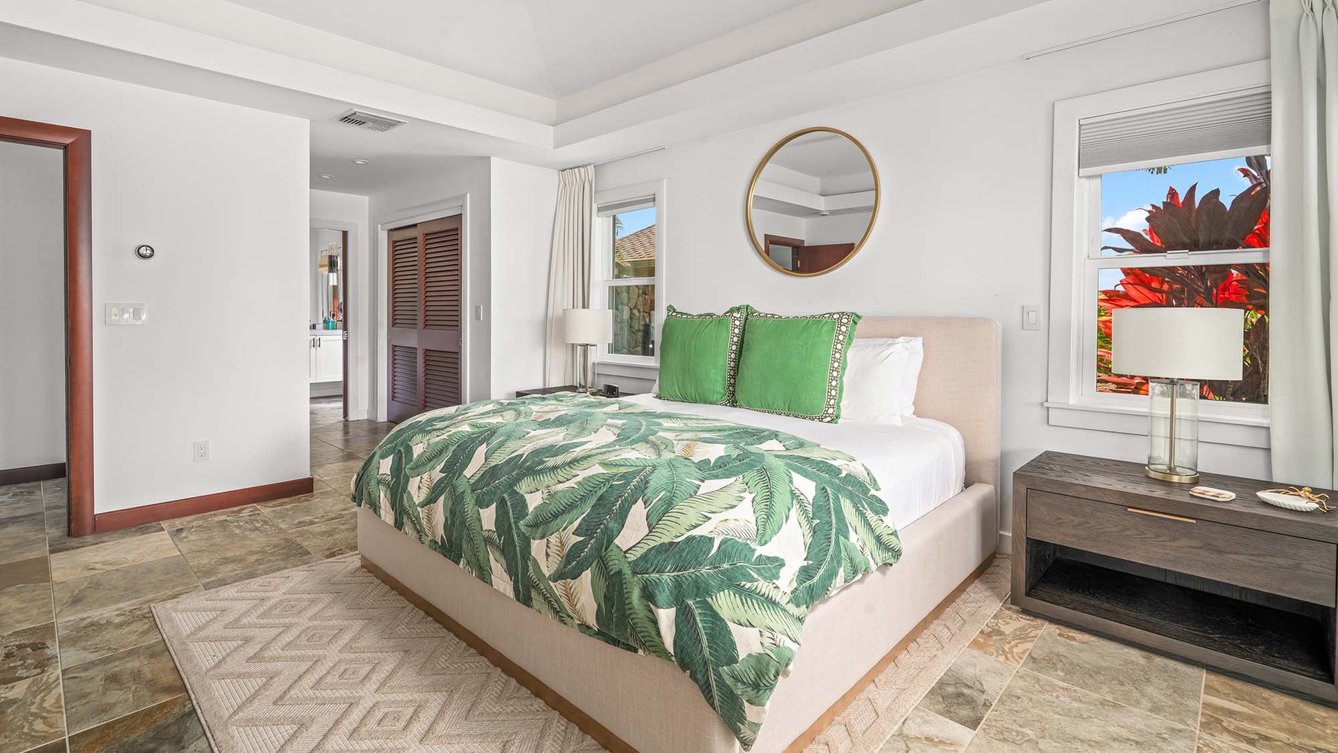 Drift off in crisp linens with tropical botanical prints, where warm wooden finishes and a round mirror above the bed create a serene, island-inspired retreat.