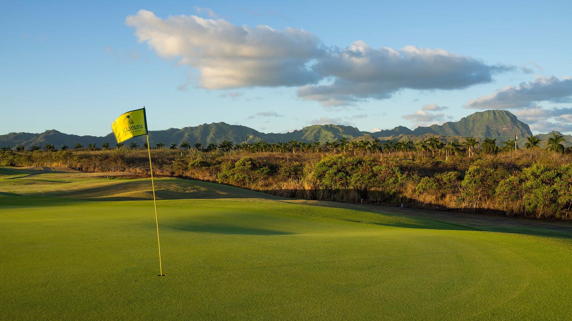 Championship golf course featuring manicured greens with dramatic mountain backdrop and tropical landscape setting.