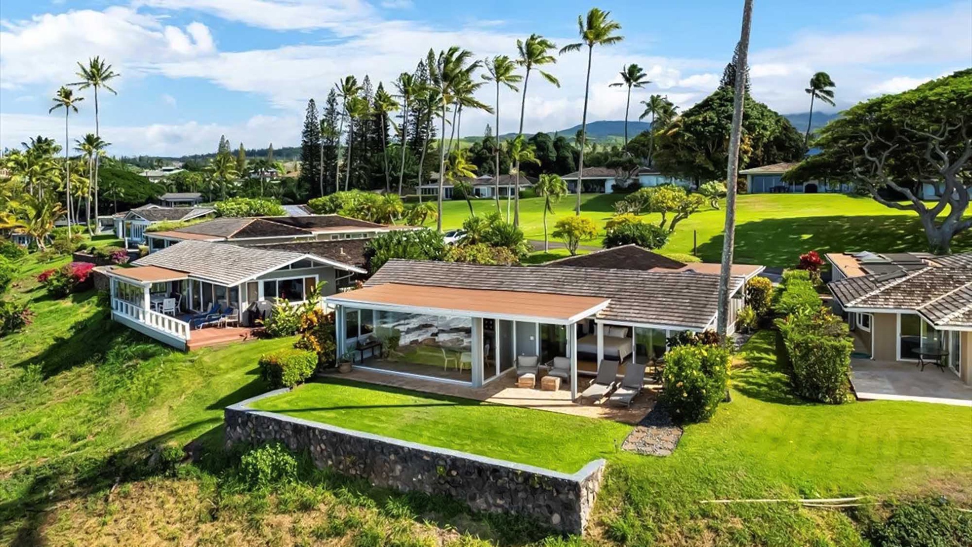 Aerial view of tropical property surrounded by lush green lawns, swaying palm trees, and neighboring homes in paradise.