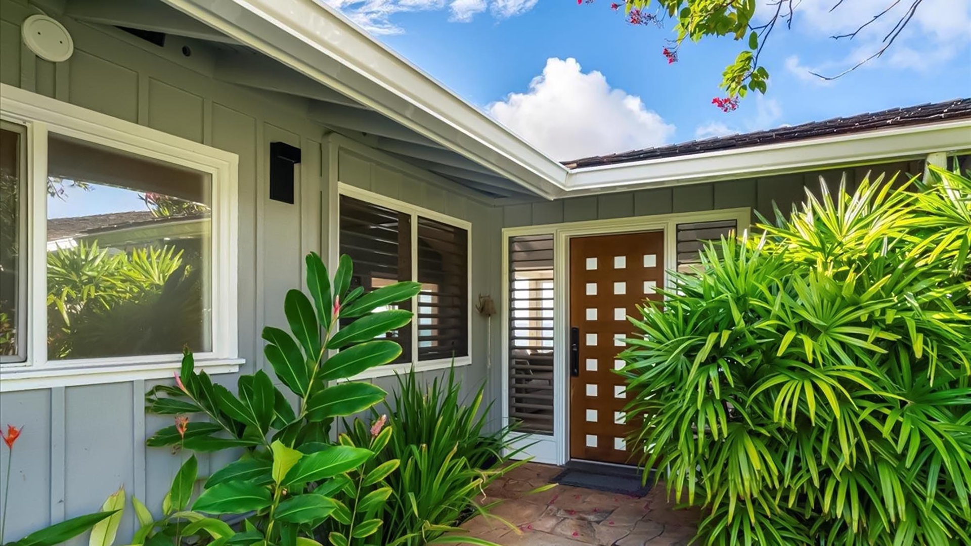 Tropical paradise surrounds this charming property entrance with lush greenery and modern design welcoming guests to their Hawaiian getaway.