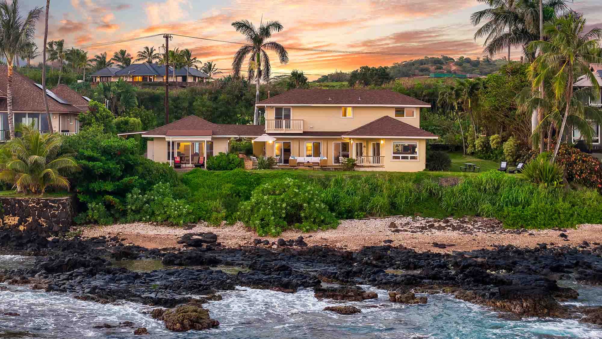This oceanfront property sits nestled between swaying palms and volcanic rock shores, with vibrant sunset skies painting the backdrop of your tropical island escape.