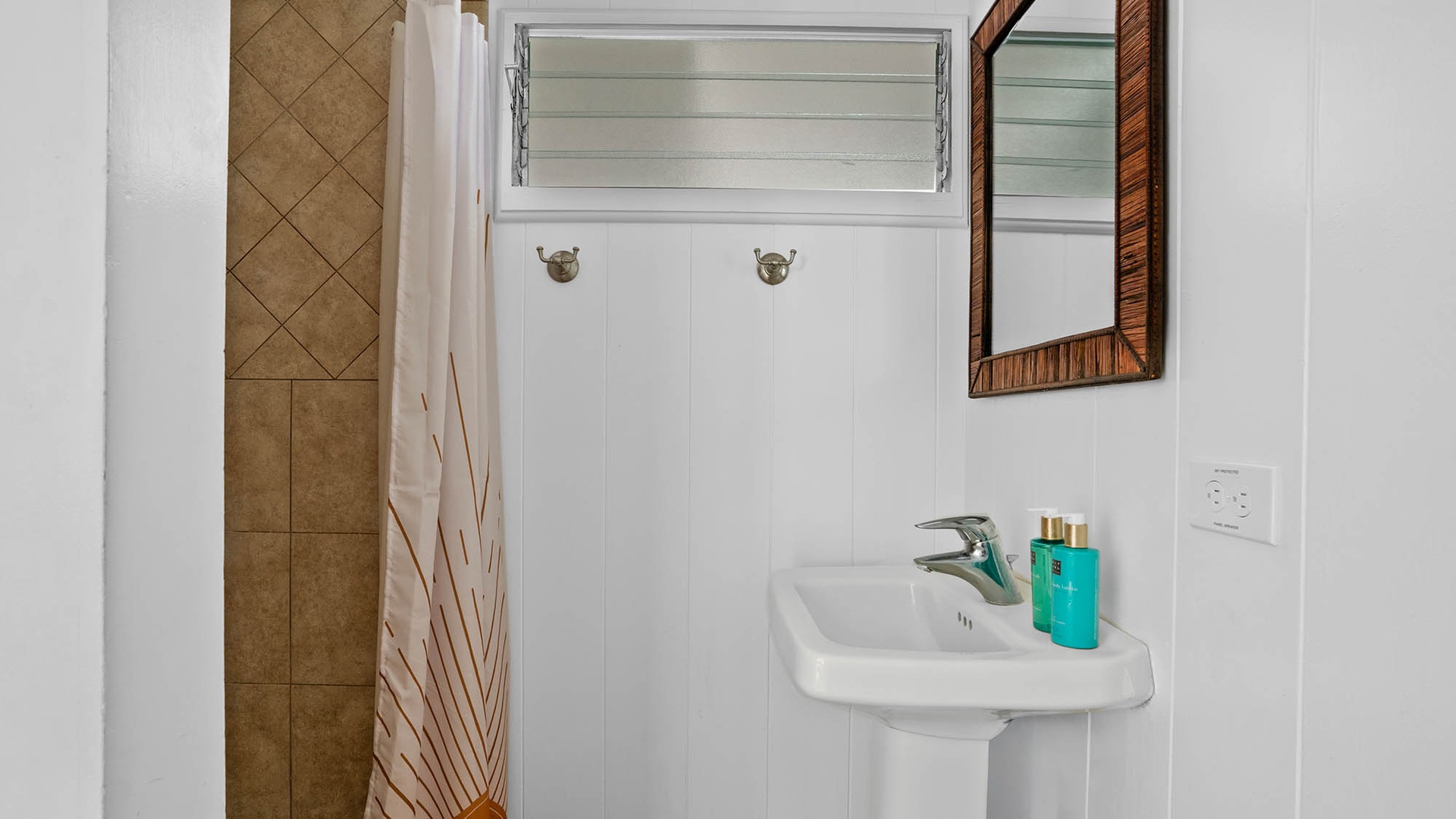 Step into your private bathroom with a sleek pedestal sink and refreshing tiled shower, where coastal cottage charm meets modern comfort.