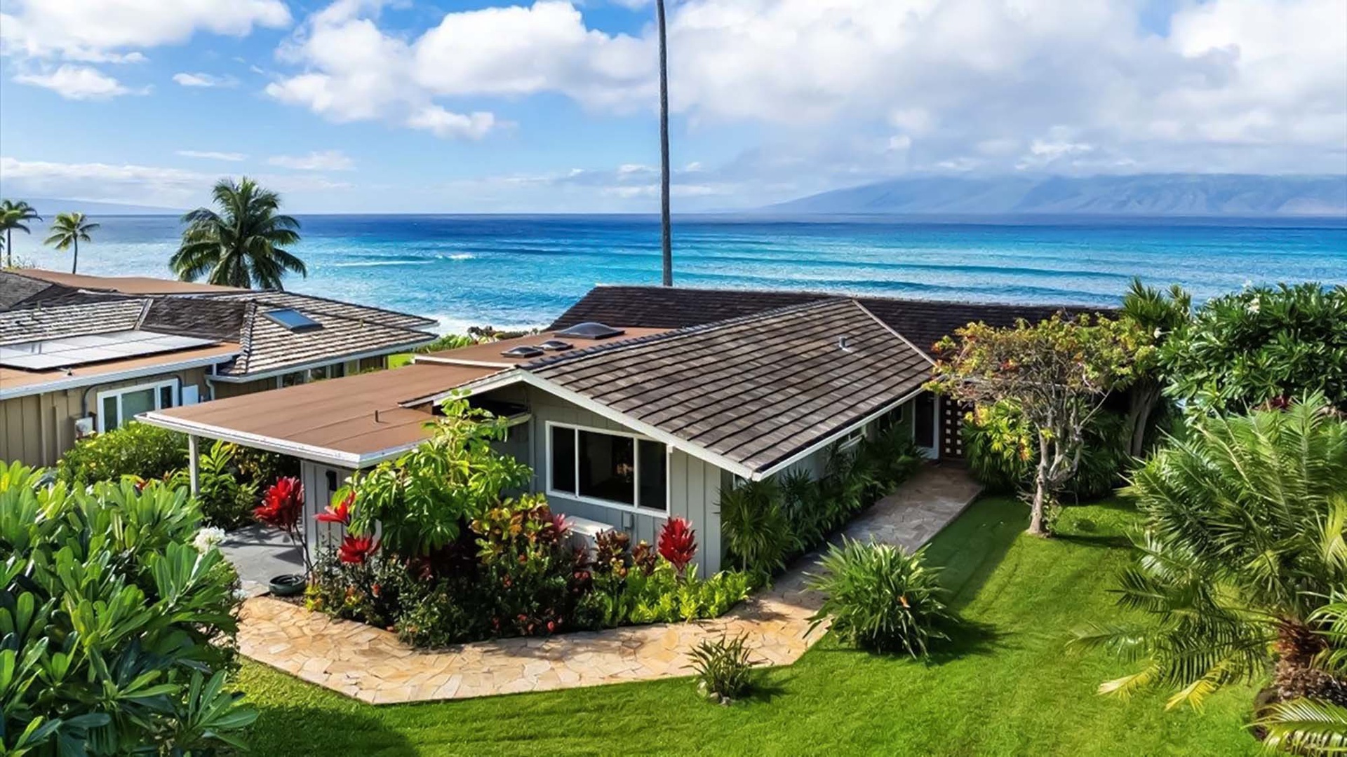 Beachfront property nestled among tropical gardens with stunning ocean views and mountain backdrop on the horizon.