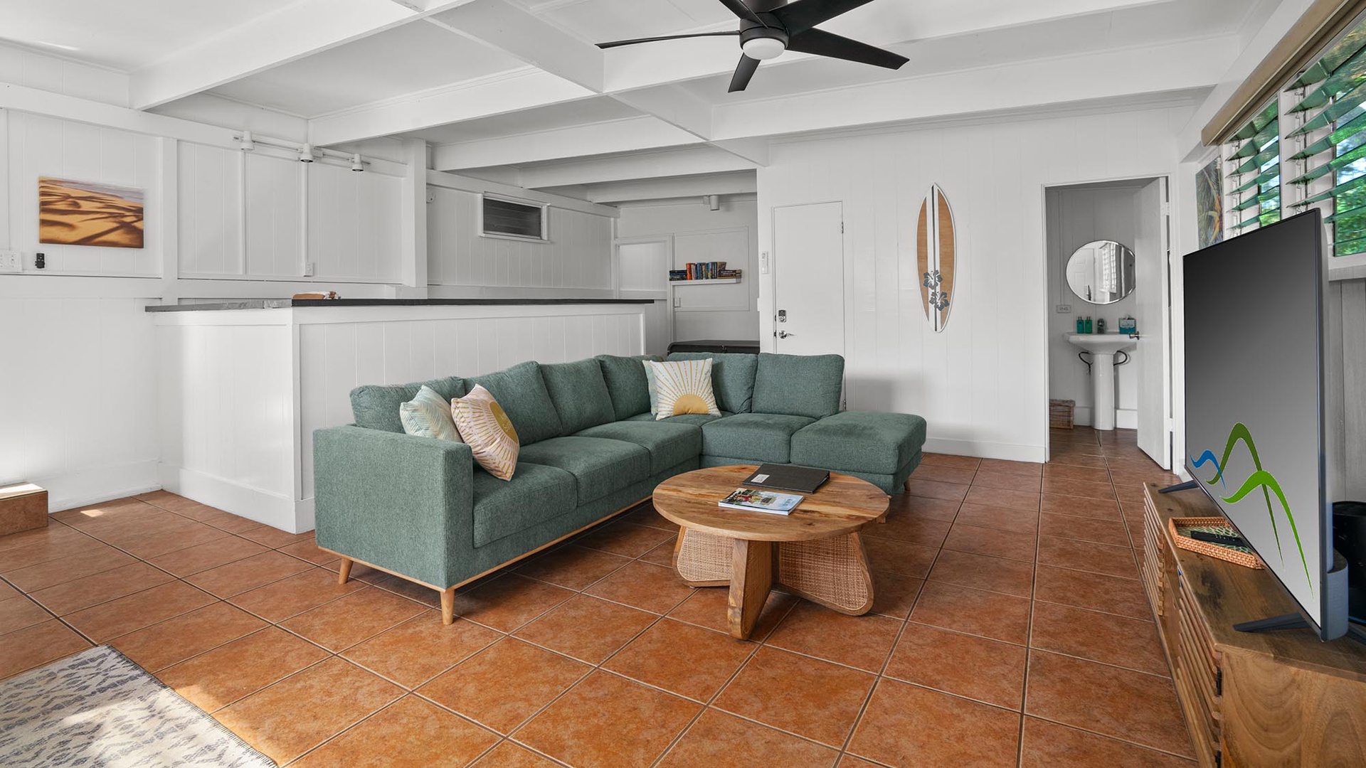 Unwind in your bright, open-plan living space with coastal touches and relaxed modern style. Settle into the comfy teal sectional, feel the cool tile beneath your feet, and enjoy the gentle breeze from the overhead fan.