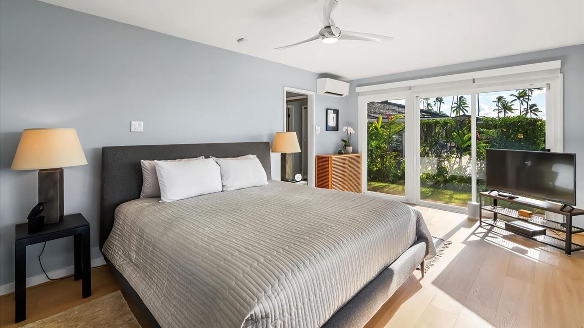 Unwind in your serene bedroom with garden views, where tropical breezes flow through sliding doors and modern comforts await your peaceful retreat.