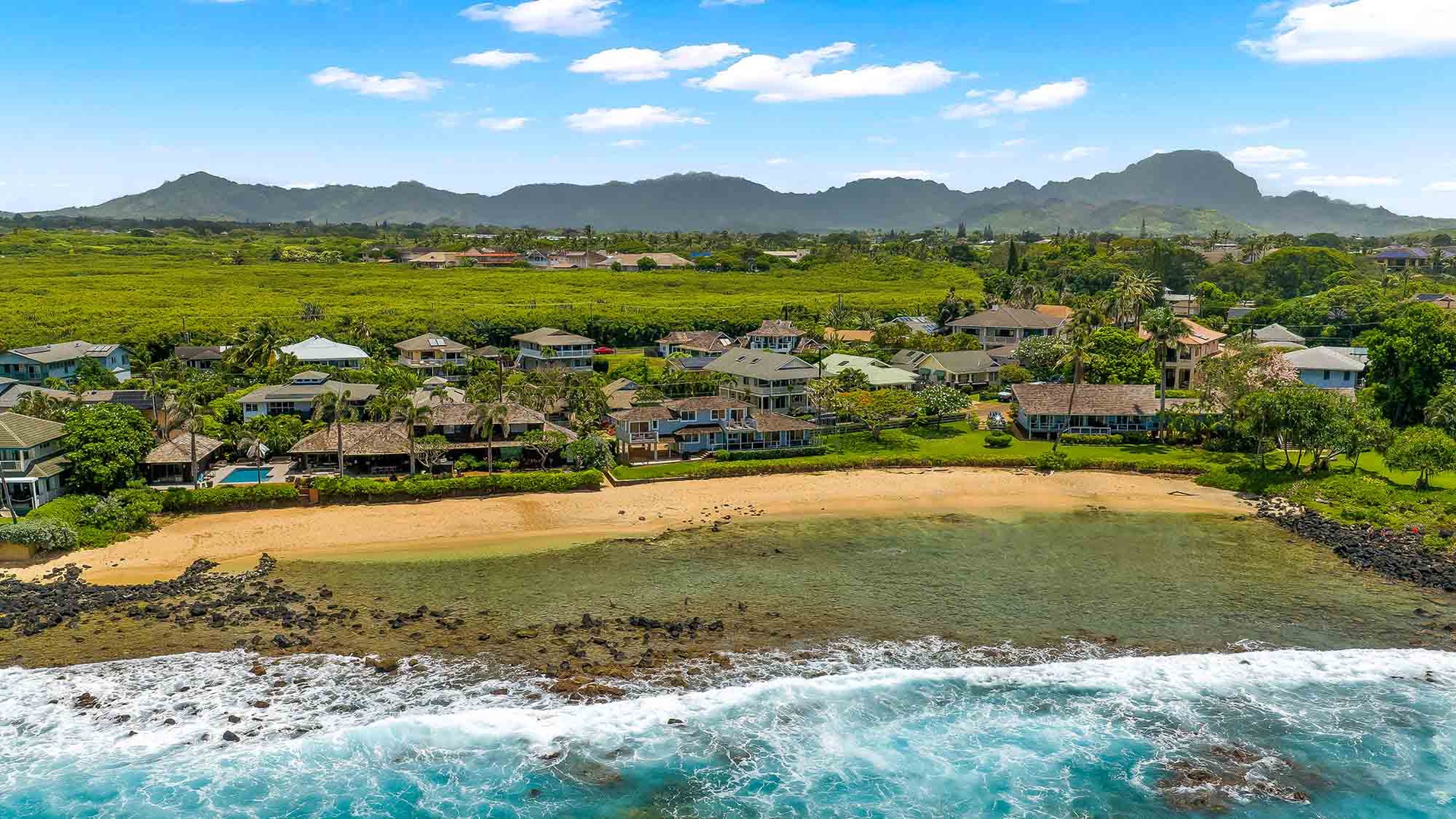 Beachfront vacation rental nestled along a golden sandy shore, with lush green landscapes and dramatic mountain views framing the peaceful coastal setting.