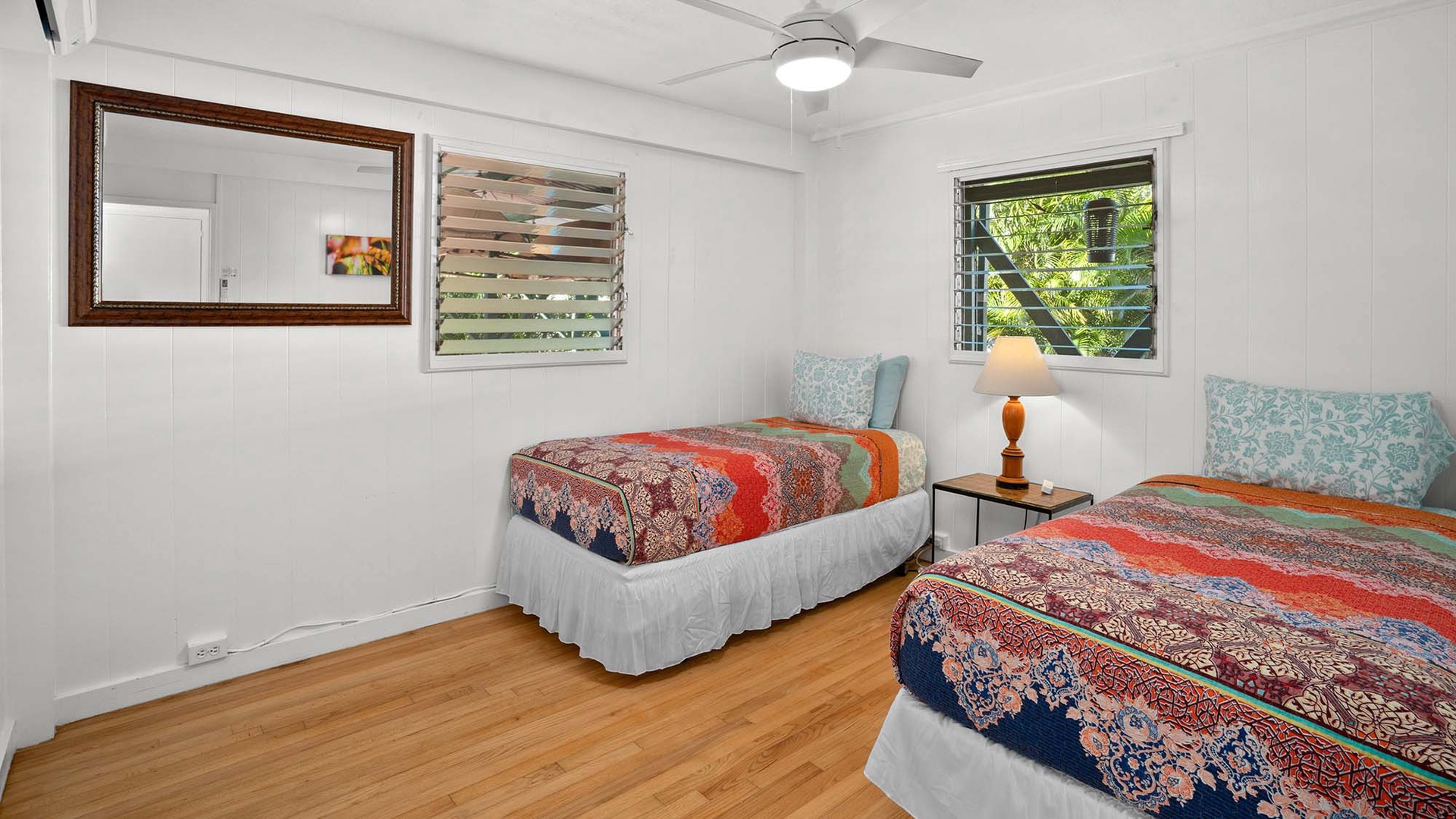 Sleep peacefully in your twin bedroom with colorful quilts, ceiling fan, and tropical garden views through louvered windows.