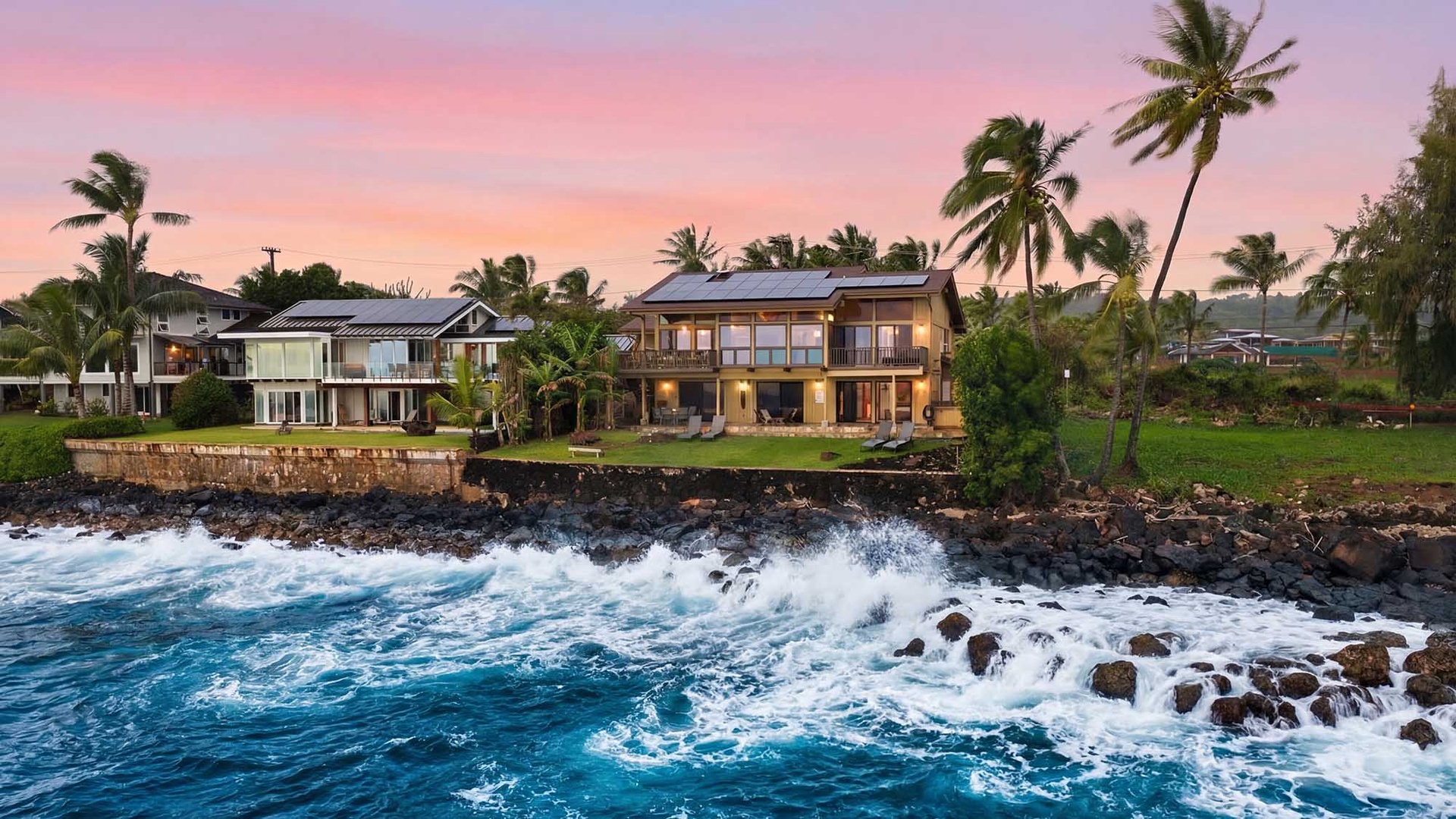 Stunning oceanfront properties with swaying palms showcase dramatic waves crashing against volcanic rocks beneath a painted sunset sky.