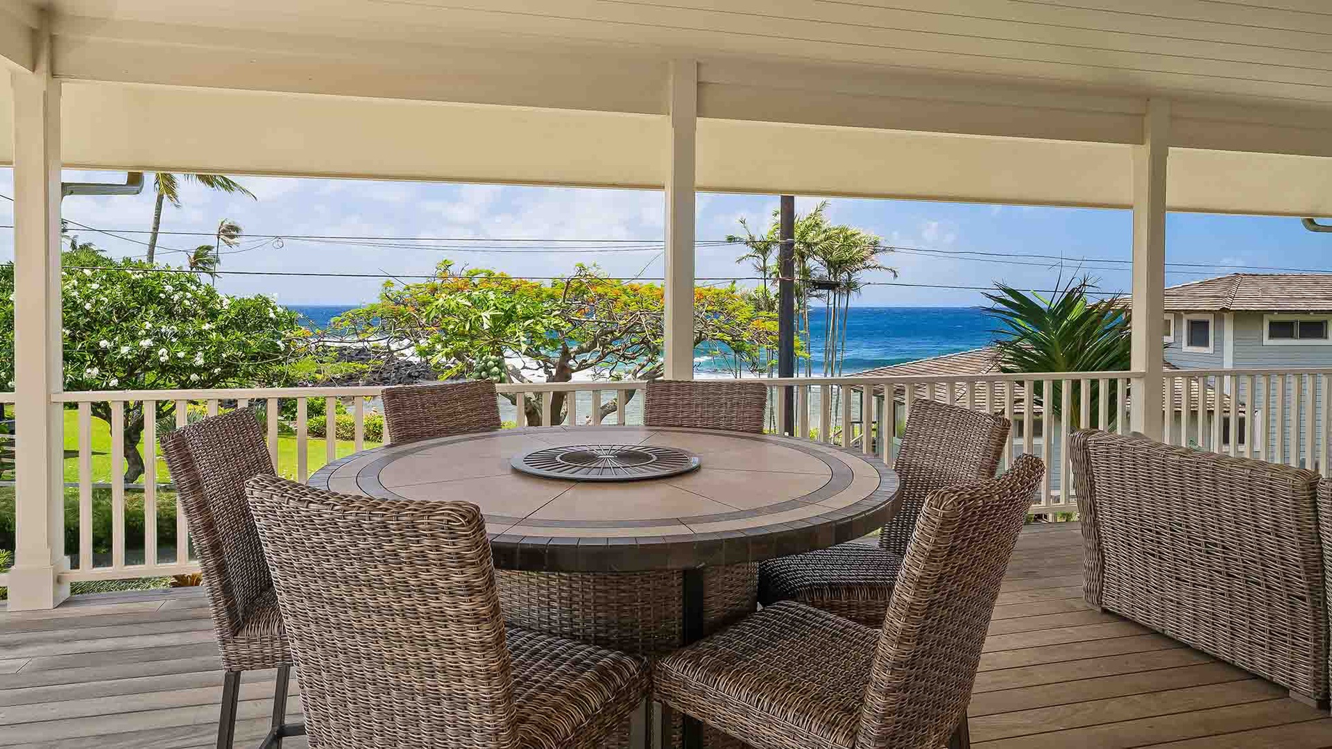 The covered lanai overlooks lush tropical greenery and sparkling blue ocean waters, offering an idyllic setting for the surrounding neighborhood.