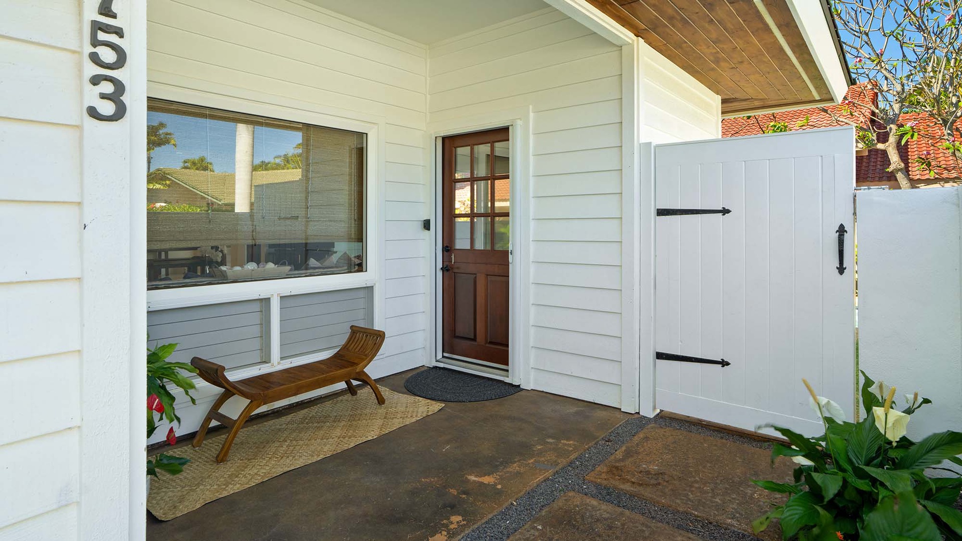 Charming cottage entrance with a welcoming wooden bench and coastal-inspired pathway framed by lush greenery and warm wood accents.
