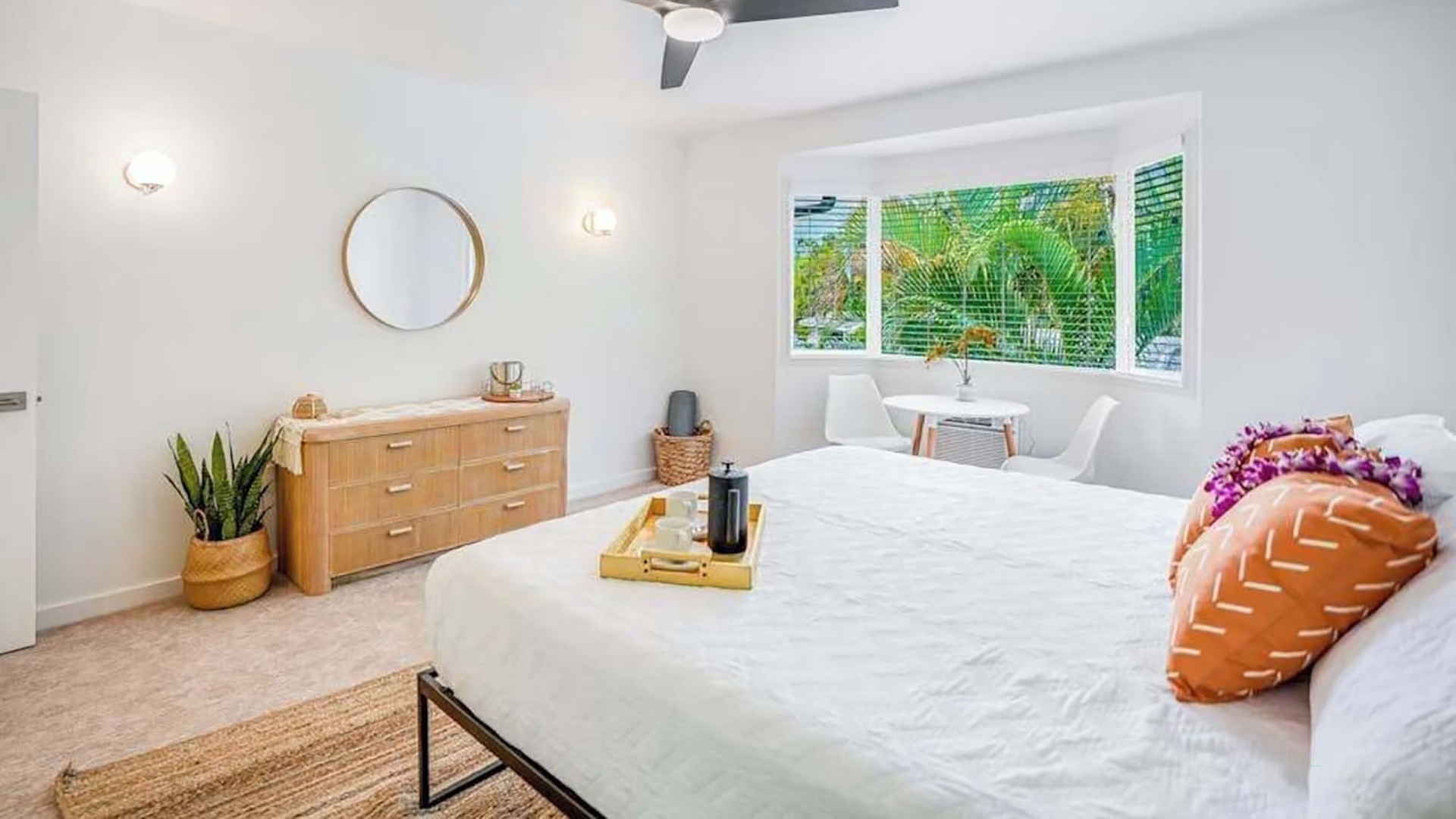 Relax in your peaceful bedroom with a plush king bed, warm natural light, and tropical garden views peeking through the window. A cozy ceiling fan keeps you cool, while the clean lines and soft touches create a calming retreat.