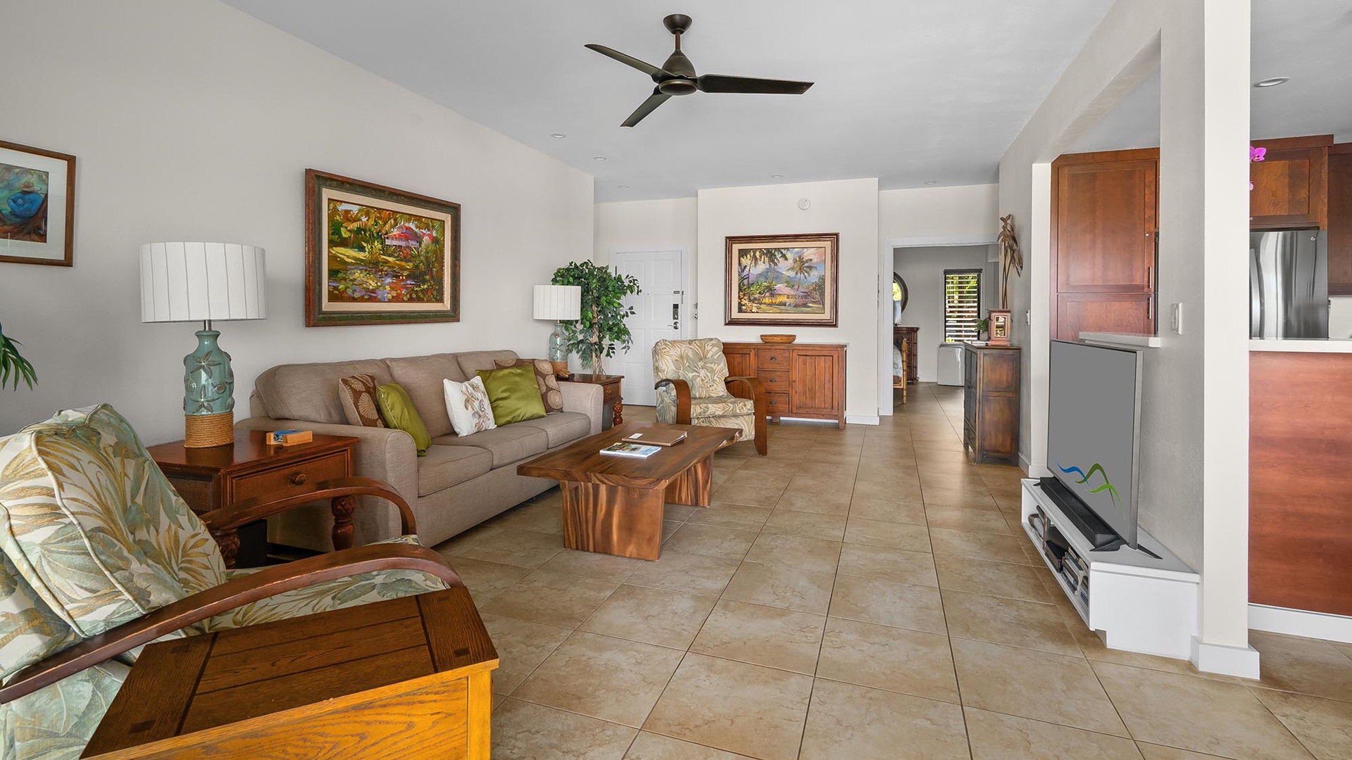 Your spacious living room welcomes you with warm wood accents, comfortable seating, and vibrant tropical artwork. Relax on plush sofas under the ceiling fan, or settle into the cozy armchair—this inviting space is perfect for unwinding after a day explori
