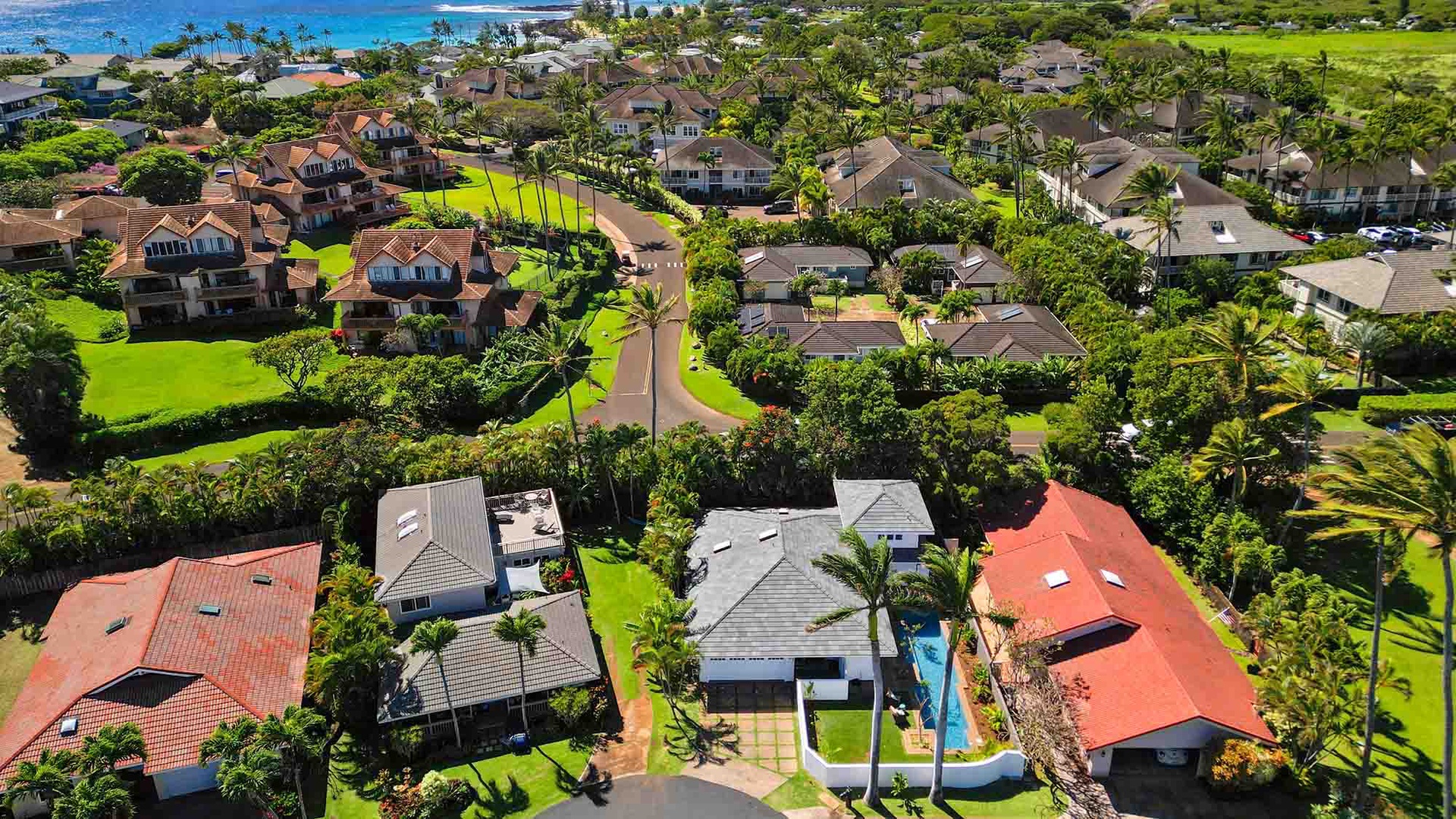 This aerial view captures the property nestled within a lush coastal neighborhood, surrounded by tropical greenery and just moments from the turquoise ocean shoreline.