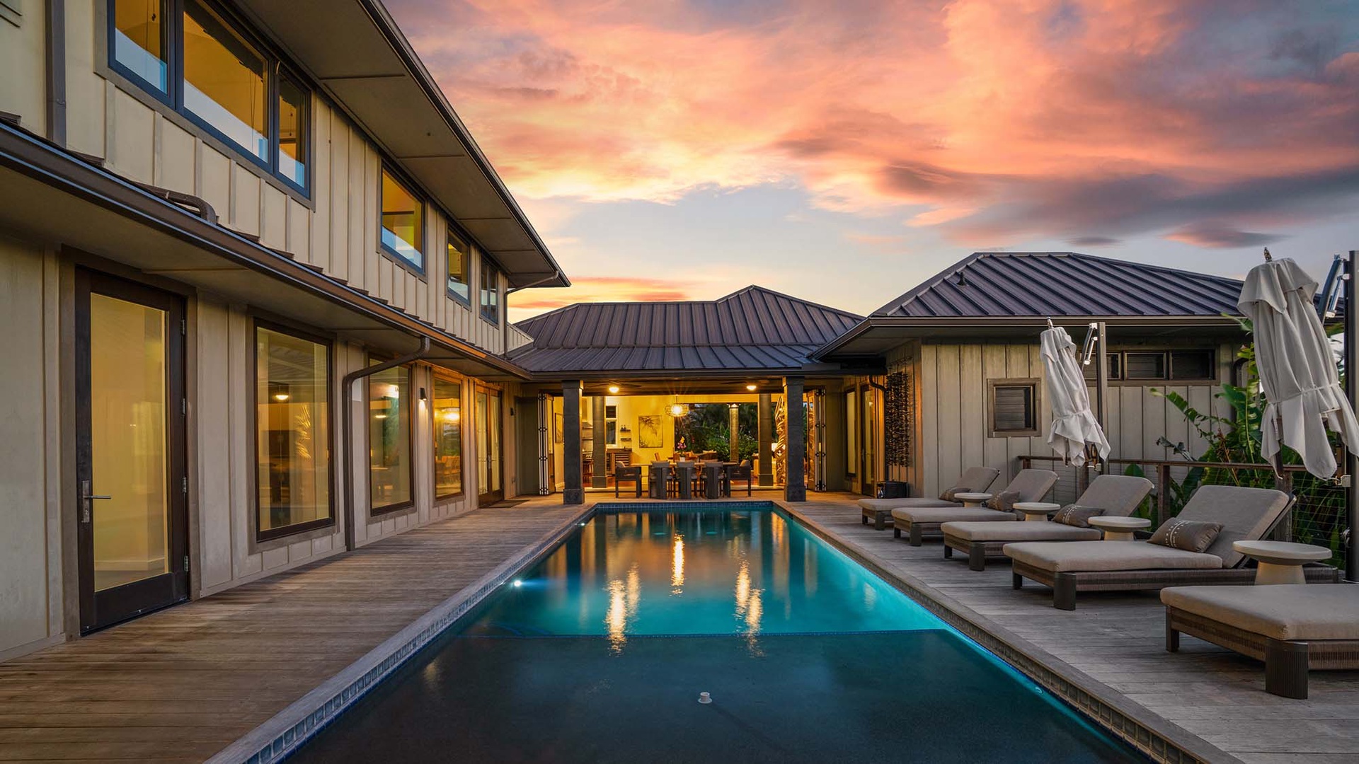 A stunning courtyard pool set against a dramatic sunset sky, bordered by elegant architecture and framed by tropical greenery defining the property's inviting outdoor centerpiece.