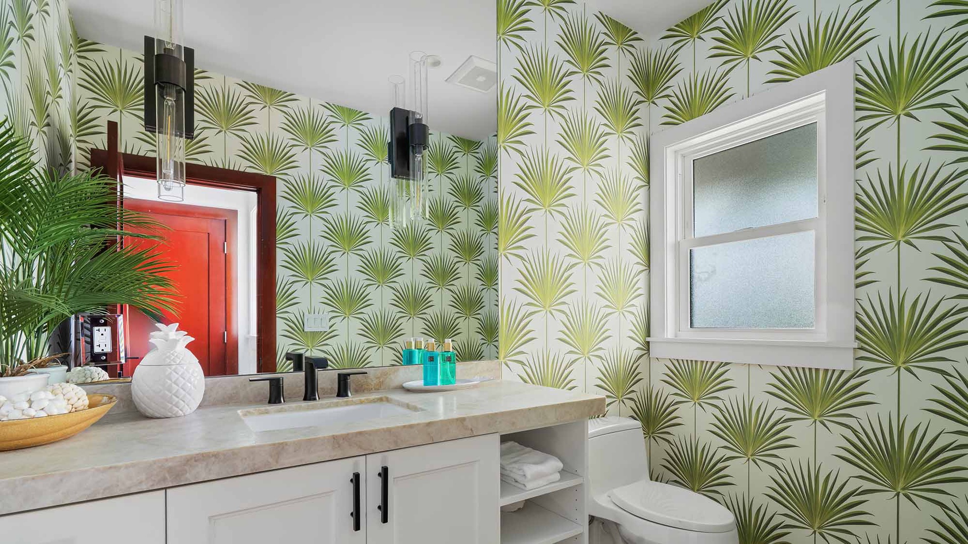 Refresh in your private bathroom featuring bold tropical wallpaper, modern fixtures, and a spacious vanity stocked with plush towels and beach-themed décor.