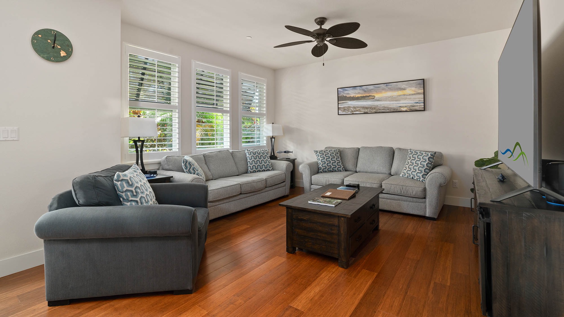 Settle into this bright, airy living room with plush sofas and warm hardwood floors. Natural light streams through plantation shutters, while a ceiling fan keeps you cool. Perfect for unwinding after island adventures.