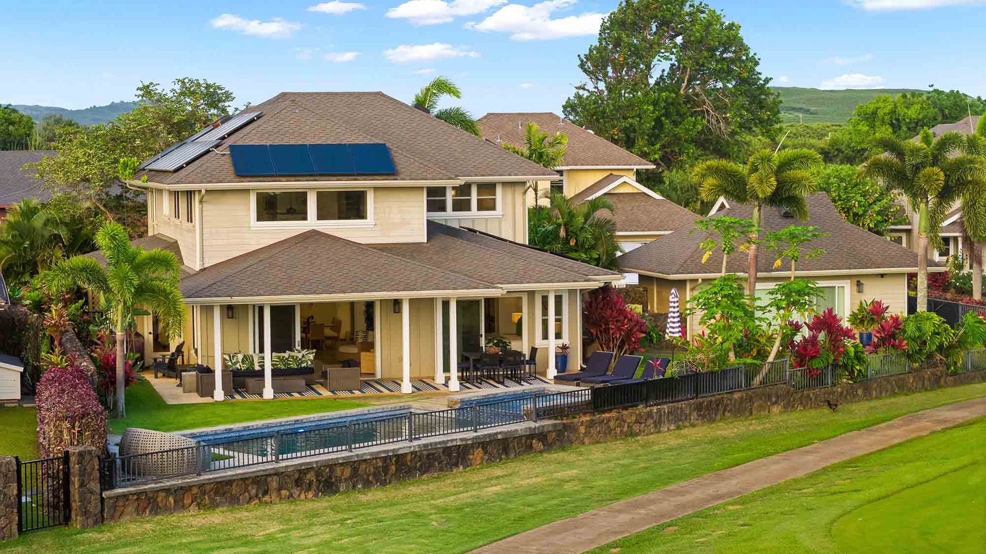 A spacious two-story Hawaiian vacation home featuring a private swimming pool, covered lanai, and lush tropical landscaping, nestled in a serene hillside neighborhood with mountain views.