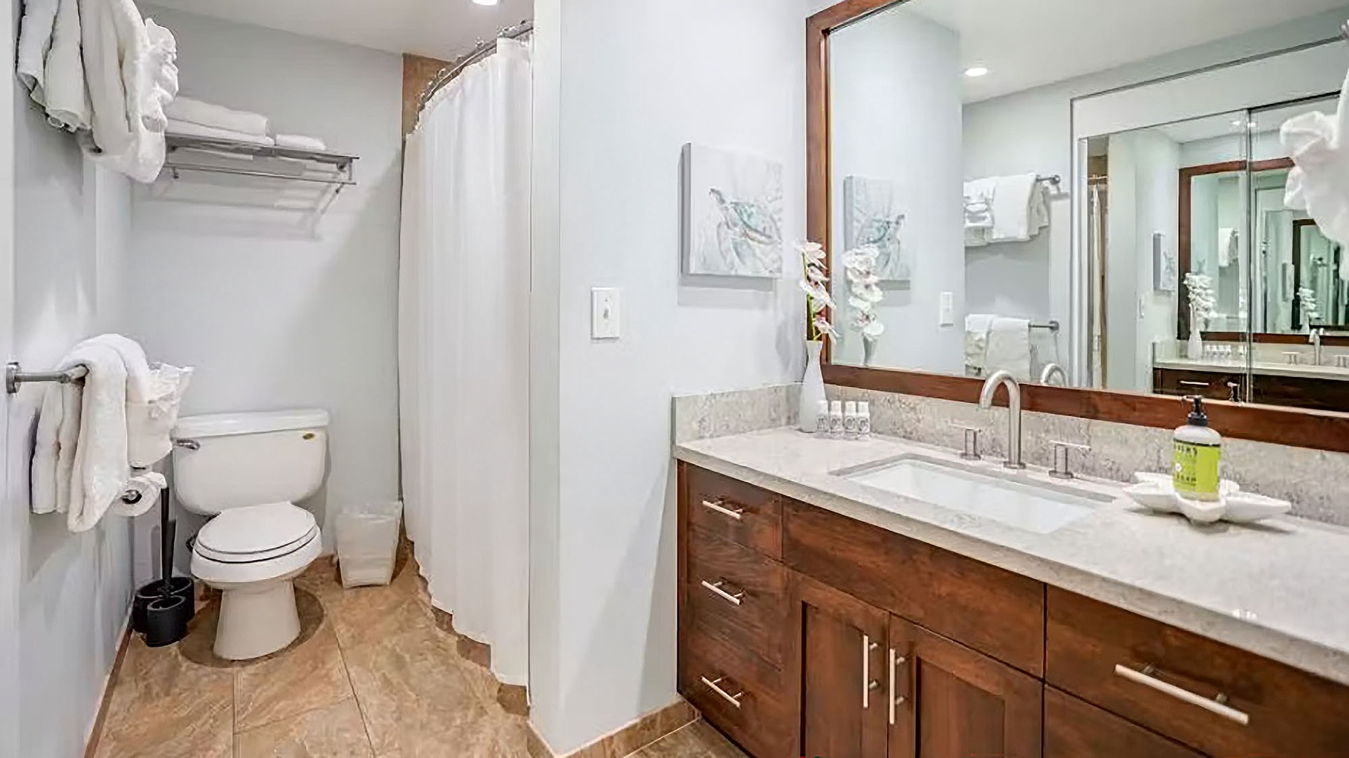 Your private bathroom features warm wood cabinetry, elegant marble countertops, and crisp white linens stacked and ready for your use—a serene retreat after a long day of exploring.