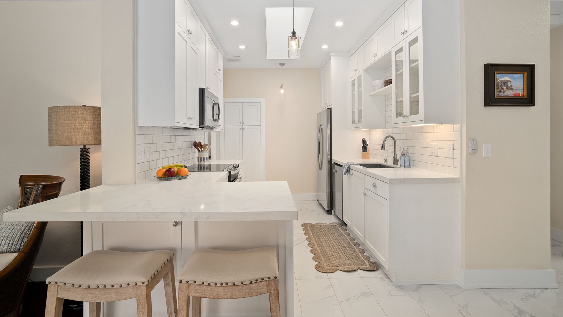 Step into your fully equipped kitchen, where sleek white cabinetry and modern appliances await. Fresh fruit on the counter and warm lighting make it easy to imagine preparing meals in this bright, inviting space.