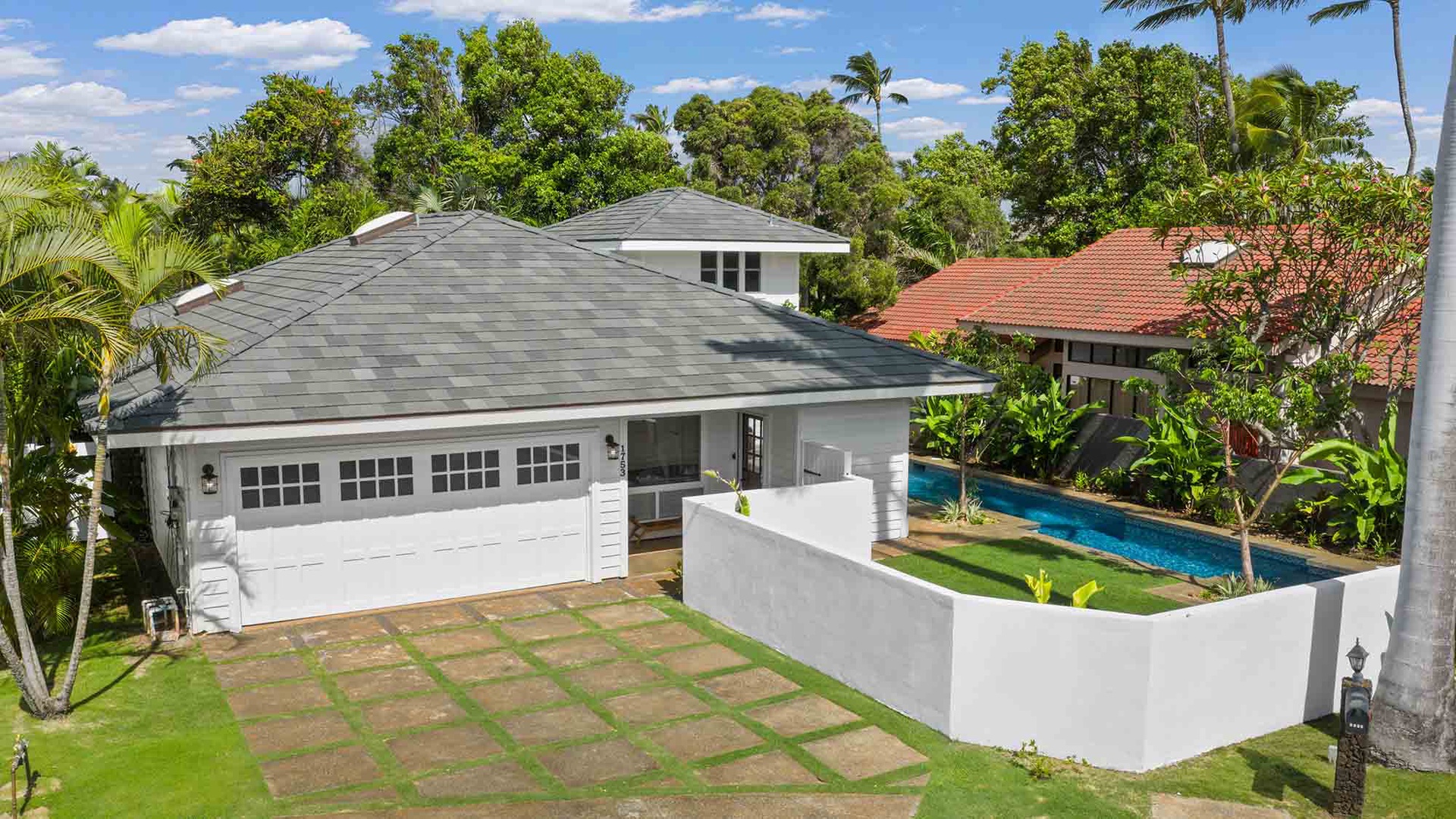 Modern vacation home nestled in a lush tropical neighborhood, featuring a private pool and spacious outdoor areas surrounded by palm trees.