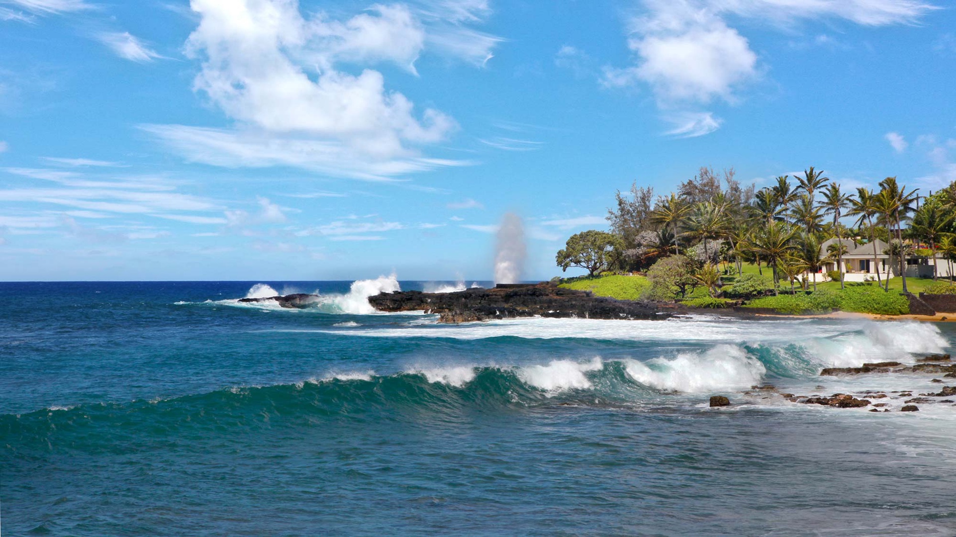 Dramatic ocean waves crash against volcanic rocks near tropical beachfront properties with swaying palm trees and lush green coastline.