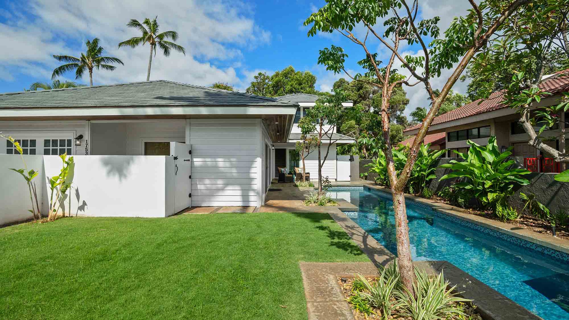 A tropical oasis awaits, with a sparkling lap pool nestled between lush green lawn and towering palms, offering your own private slice of paradise under endless blue skies.
