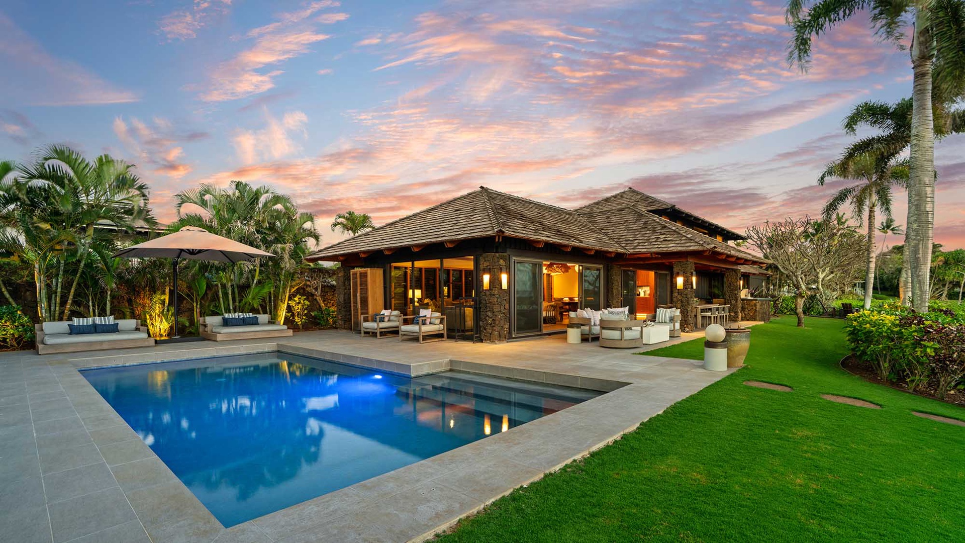 Tropical villa with private pool surrounded by lush palms under dramatic sunset skies.