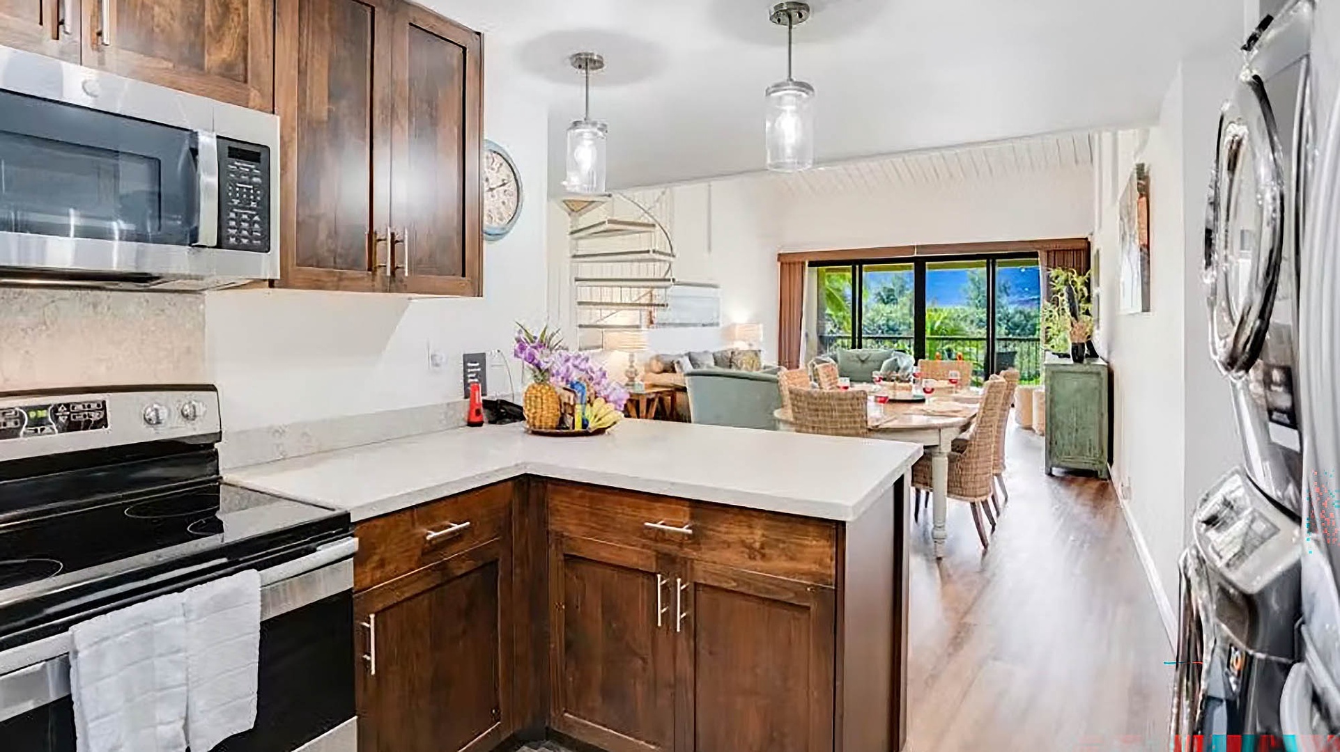 Step into your open-concept space where warm wood tones meet bright natural light. The fully equipped kitchen flows seamlessly into the dining and living areas, framed by stunning mountain and garden views beyond.