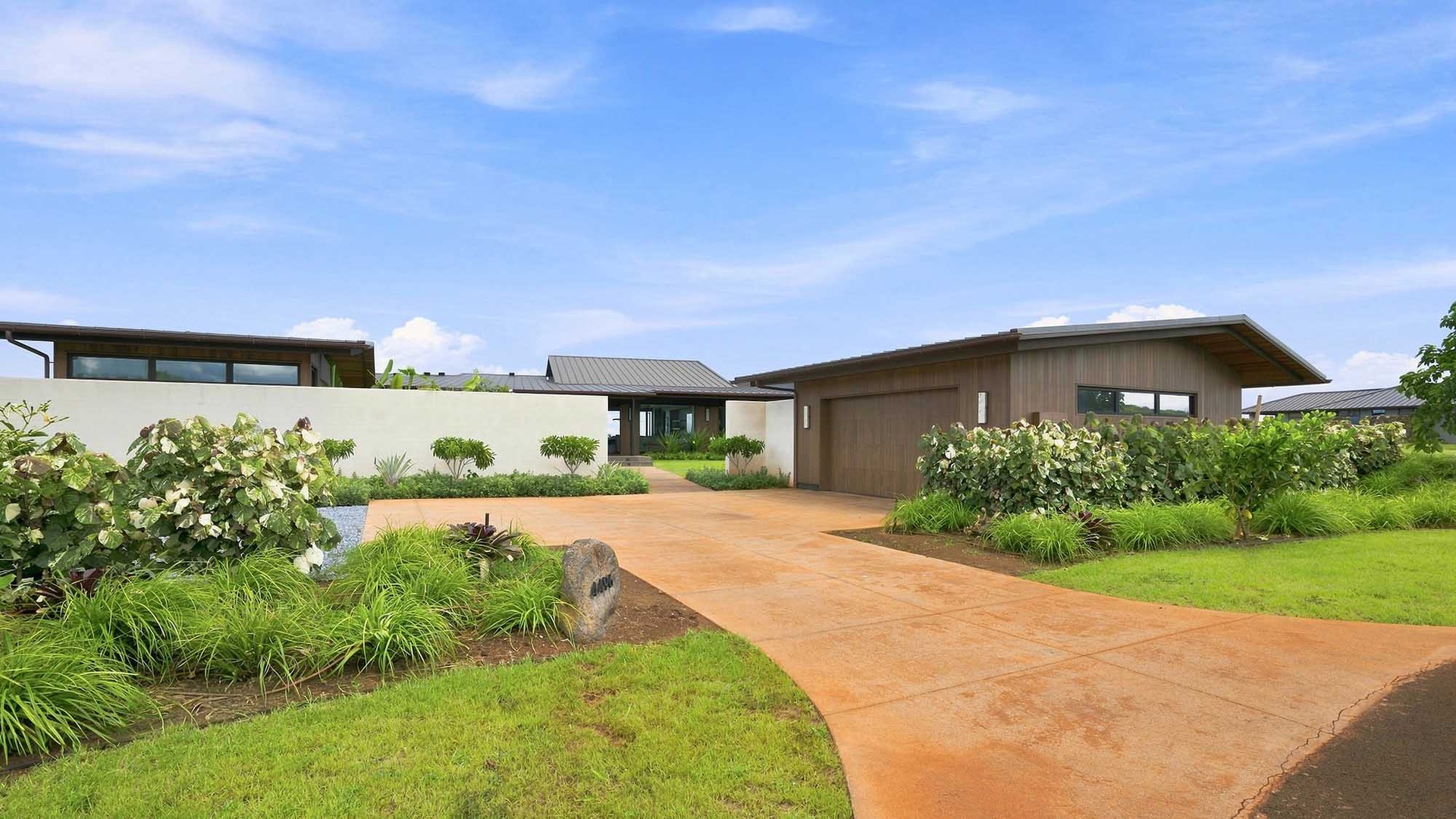 Modern architecture nestled in lush tropical landscaping features a welcoming driveway and beautifully maintained gardens surrounding the entrance.