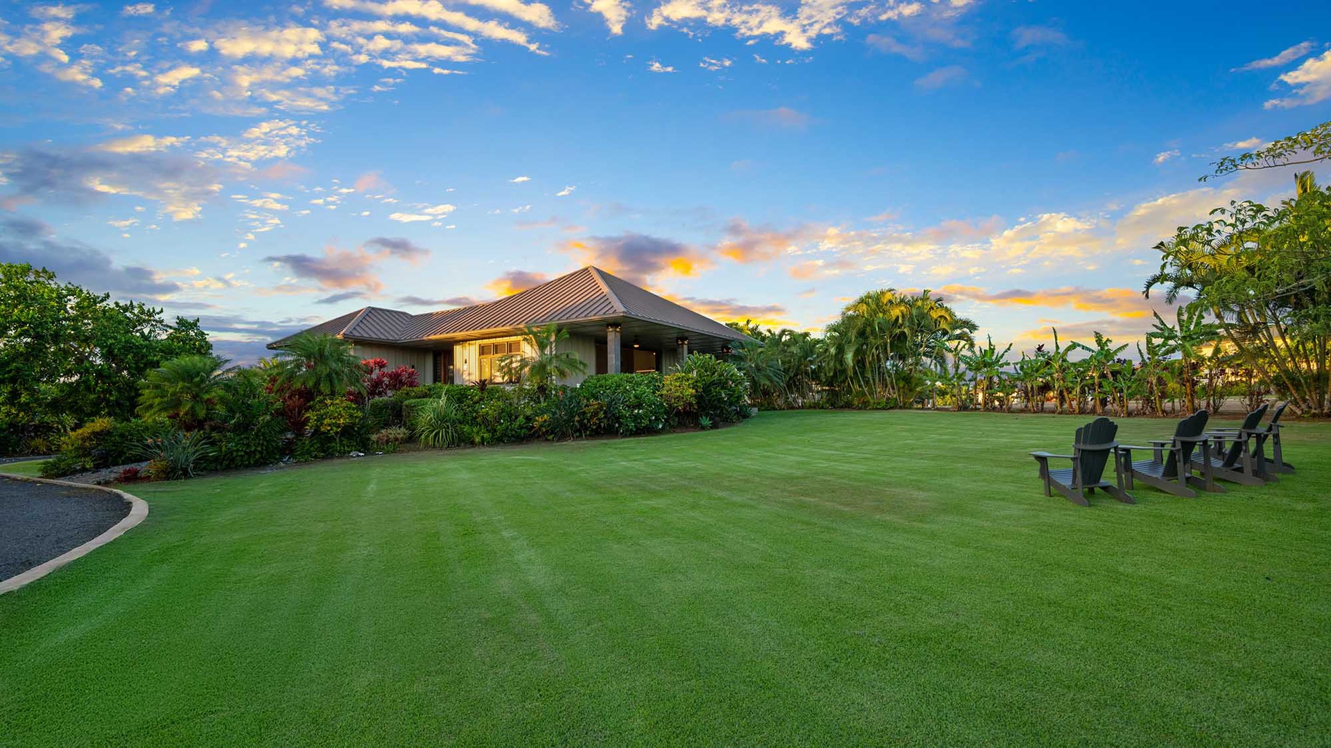 A tropical vacation property surrounded by lush landscaping and manicured lawn, set beneath a dramatic sunset sky.
