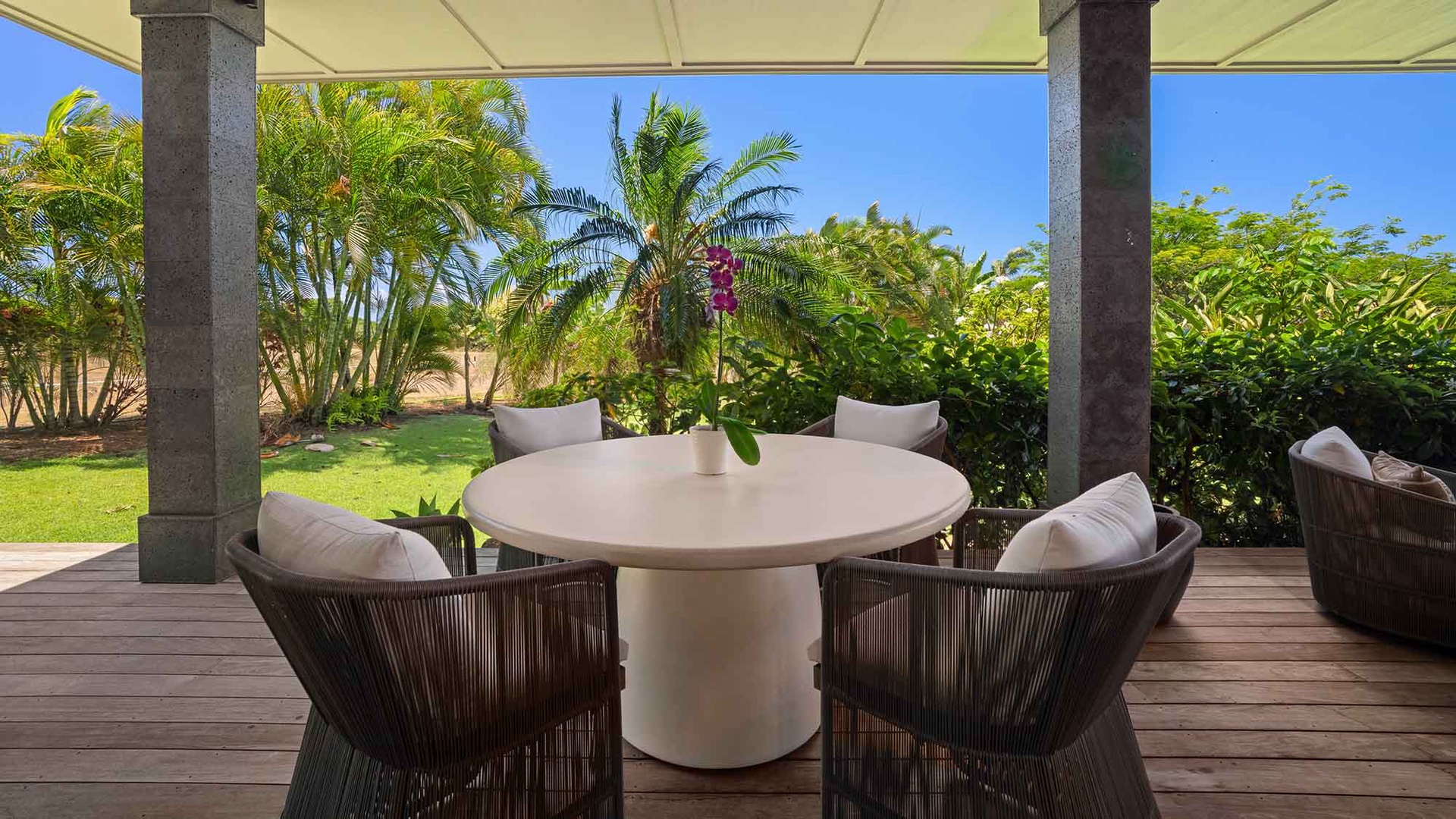 Step onto your private covered terrace where lush tropical gardens and swaying palms frame your peaceful outdoor dining space, perfect for morning coffee or sunset cocktails.