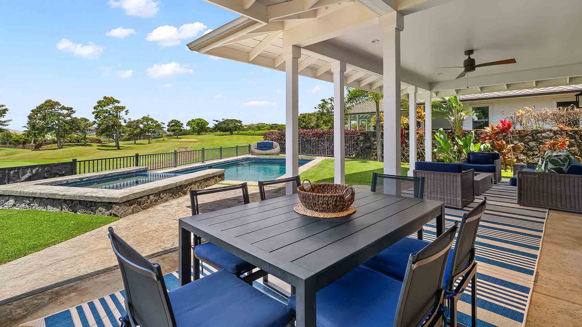 The covered patio overlooks a swimming pool and golf course, offering outdoor dining space surrounded by lush tropical landscaping and expansive green fairways.