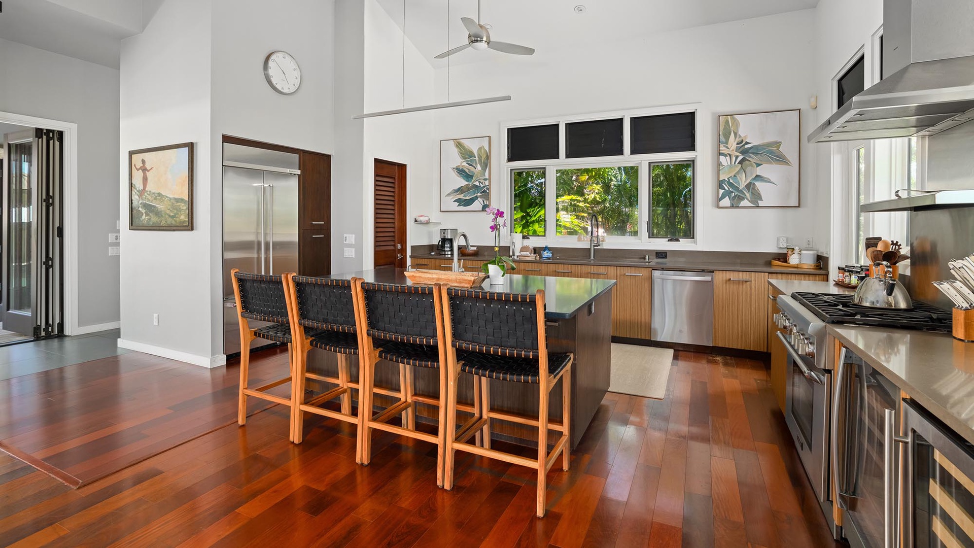 Picture yourself preparing meals in this airy, modern kitchen with gleaming stainless appliances, rich wood cabinetry, and a spacious island perfect for gathering. Natural light pours in through large windows overlooking lush greenery.
