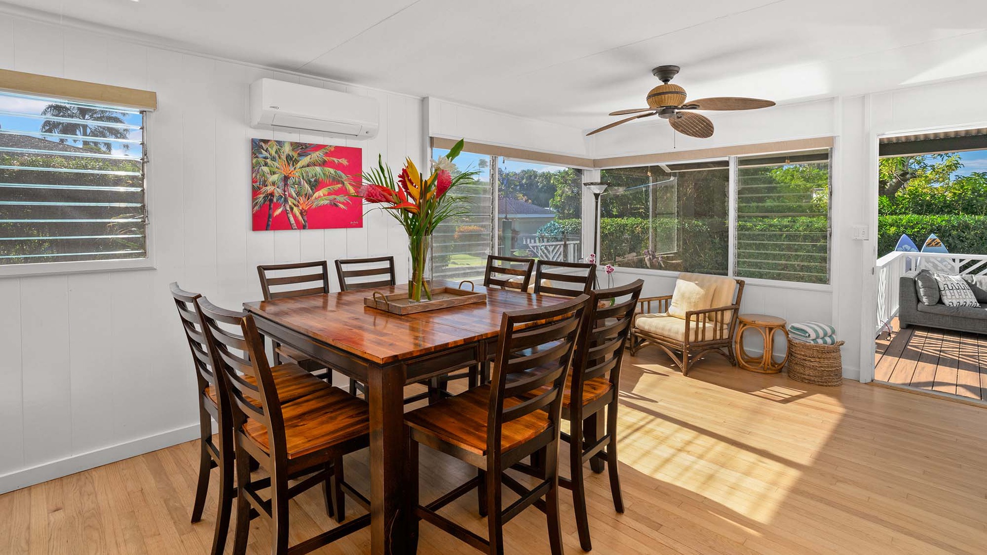 Gather around this warm wooden dining table where tropical blooms and sunlit windows create the perfect setting for memorable meals together.