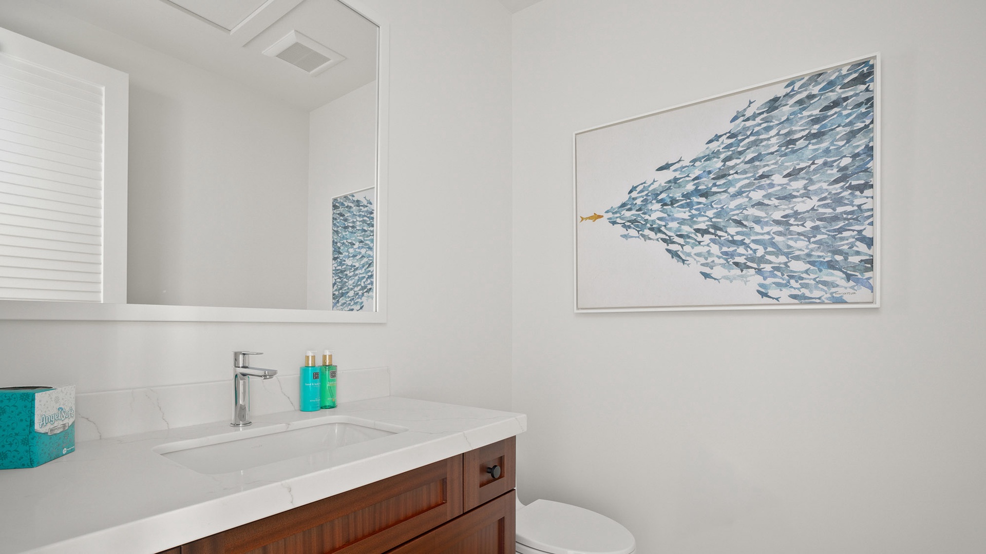 Your powder room combines modern elegance with coastal charm, featuring serene fish artwork and clean lines for a refreshing retreat.