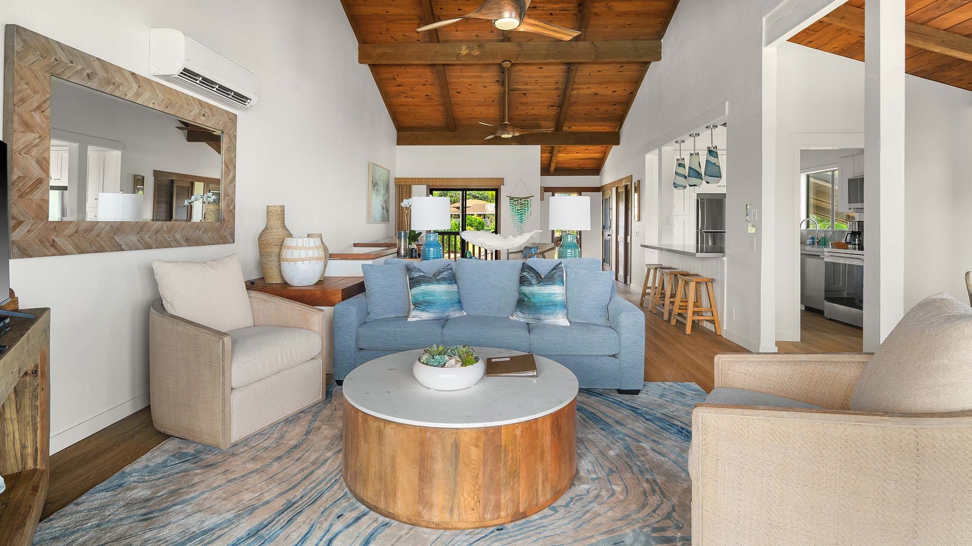 Relax in your spacious living room featuring vaulted wood ceilings, coastal-inspired furnishings, and an open layout that flows seamlessly into the kitchen and dining areas—perfect for unwinding after a day of adventure.