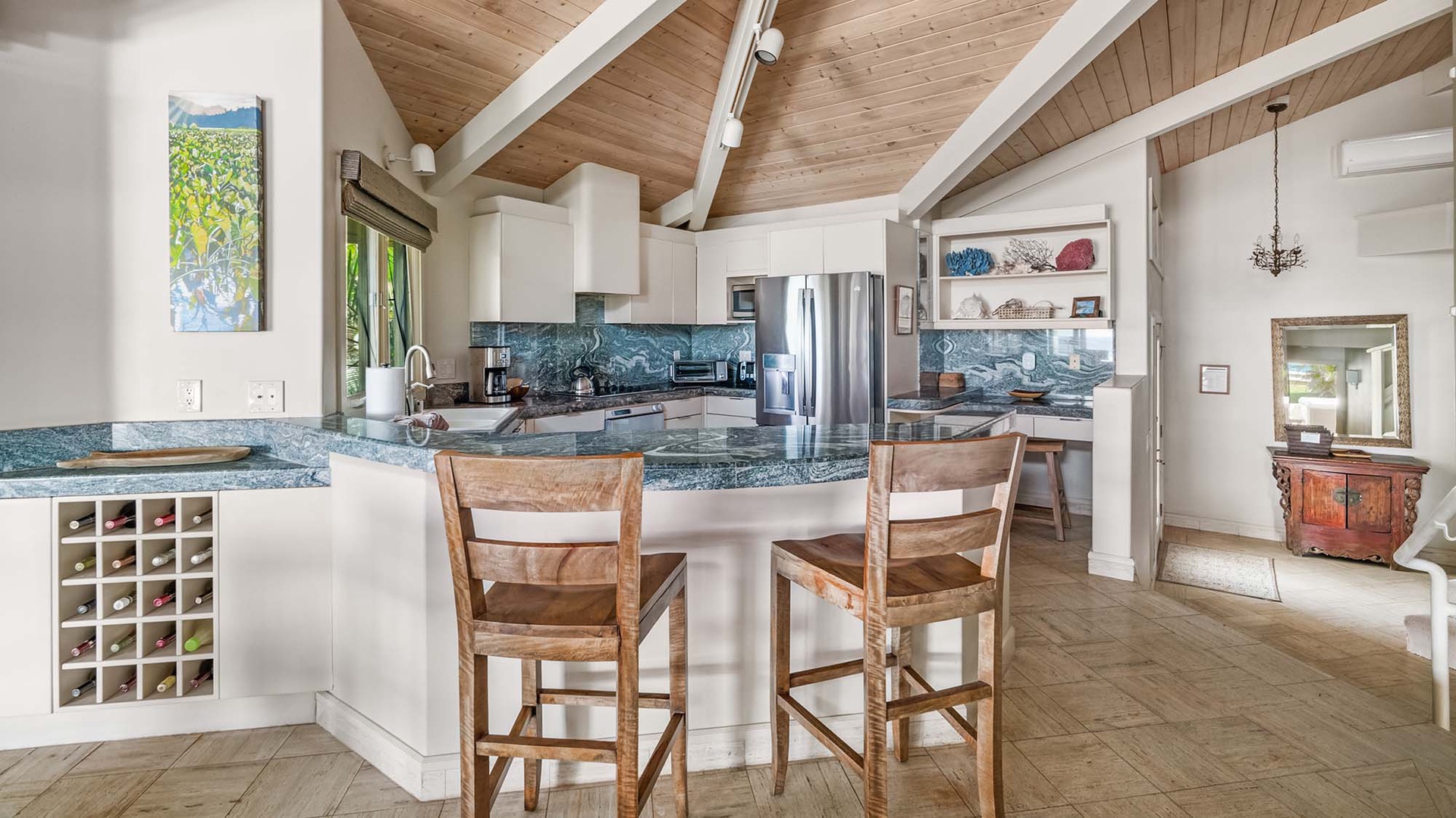 Step into your spacious gourmet kitchen with vaulted wood ceilings, gleaming granite counters, and modern stainless appliances—perfect for preparing meals while enjoying views of tropical greenery through the windows.