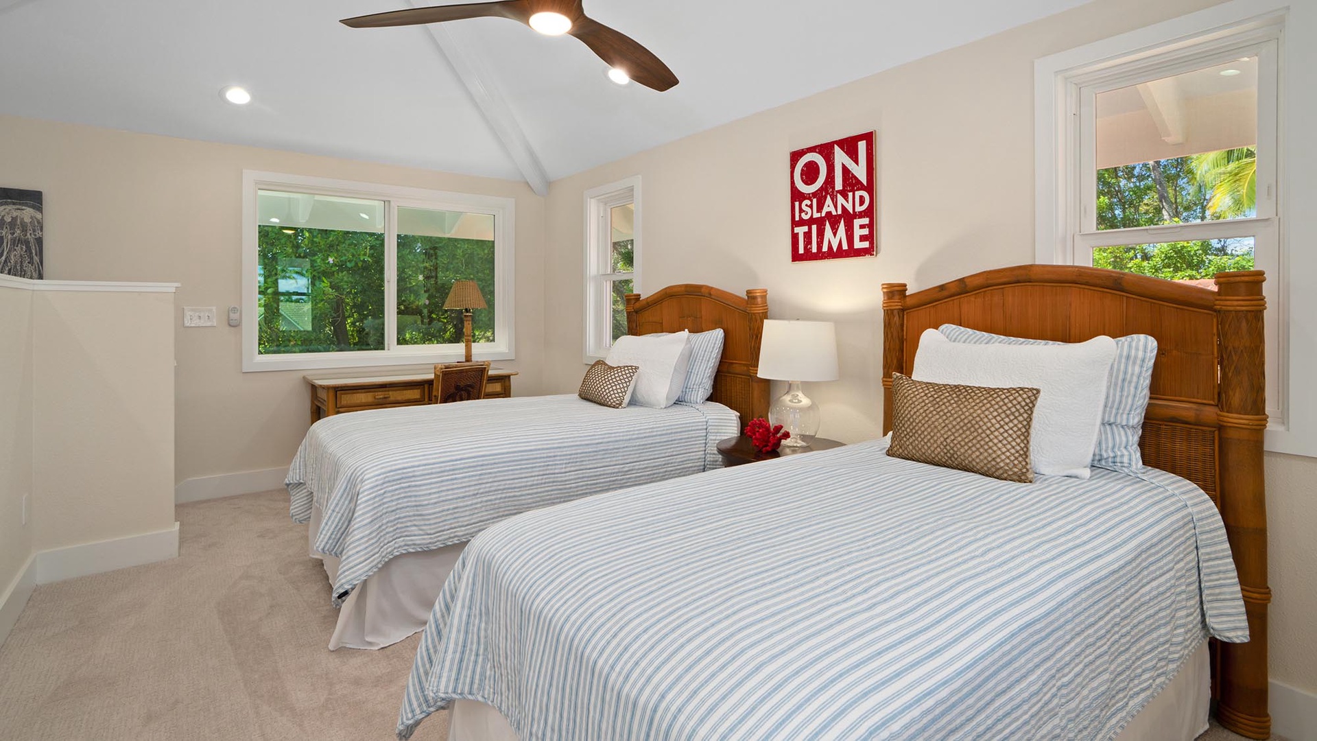 Your comfortable bedroom features two inviting beds with crisp linens and warm wood furnishings. Natural light streams through the windows, and the ceiling fan keeps the island breeze flowing throughout your stay.