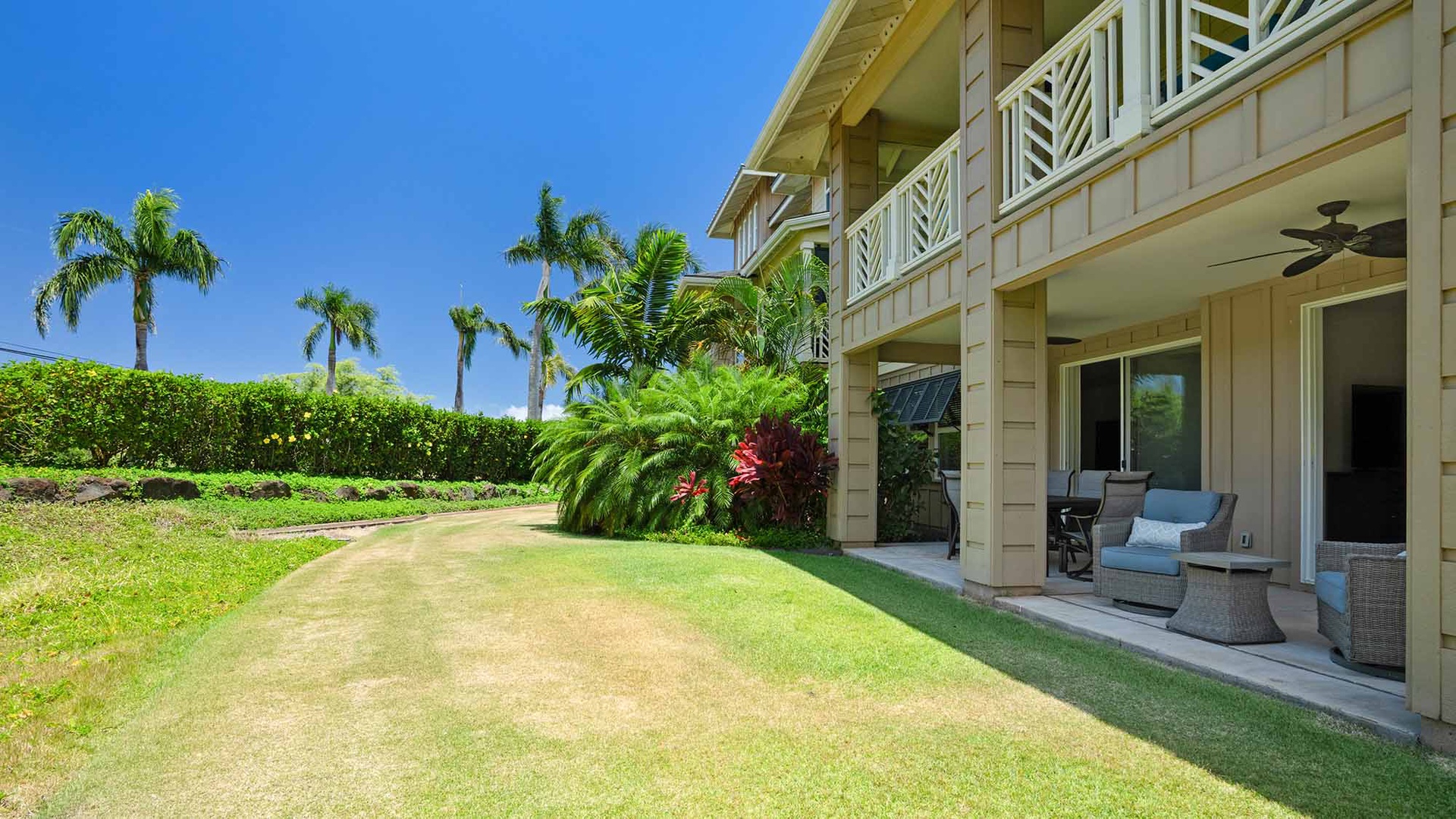 Beachside property features a spacious private lawn surrounded by tropical palms and lush hedges, with a covered patio perfect for outdoor relaxation under blue skies.